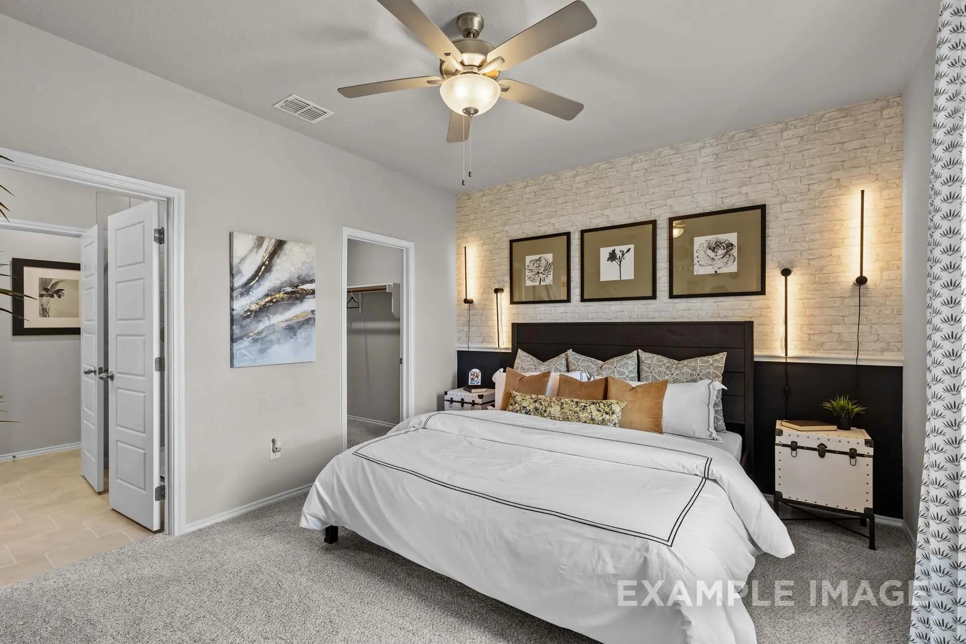 Modern primary bedroom with brick accent wall and ceiling fan in The Sabine H floor plan at Heartland, Texas.