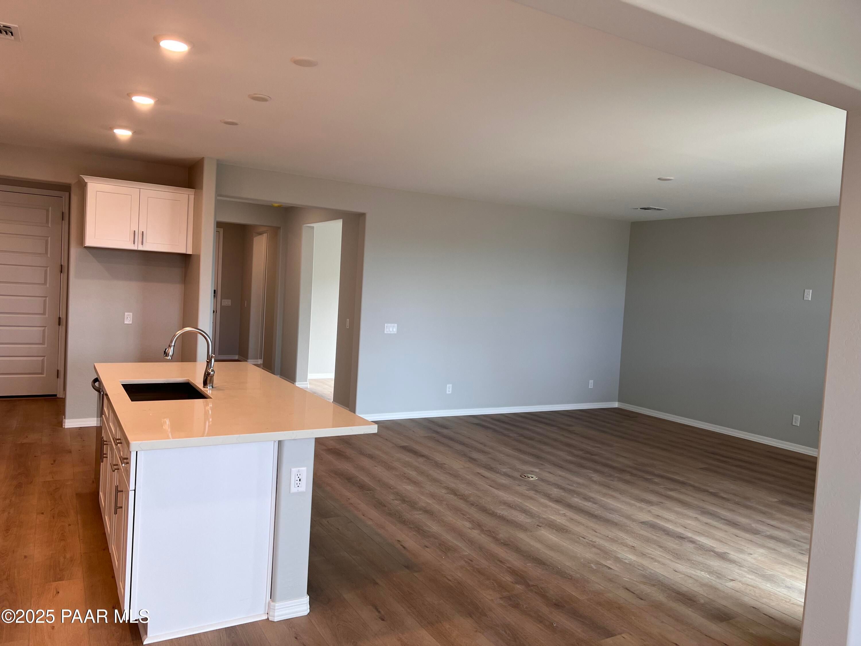 Open-concept kitchen with white cabinets, tan island sink, and wood flooring in Davidson Homes The Inspiration B, Prescott Valley, Arizona