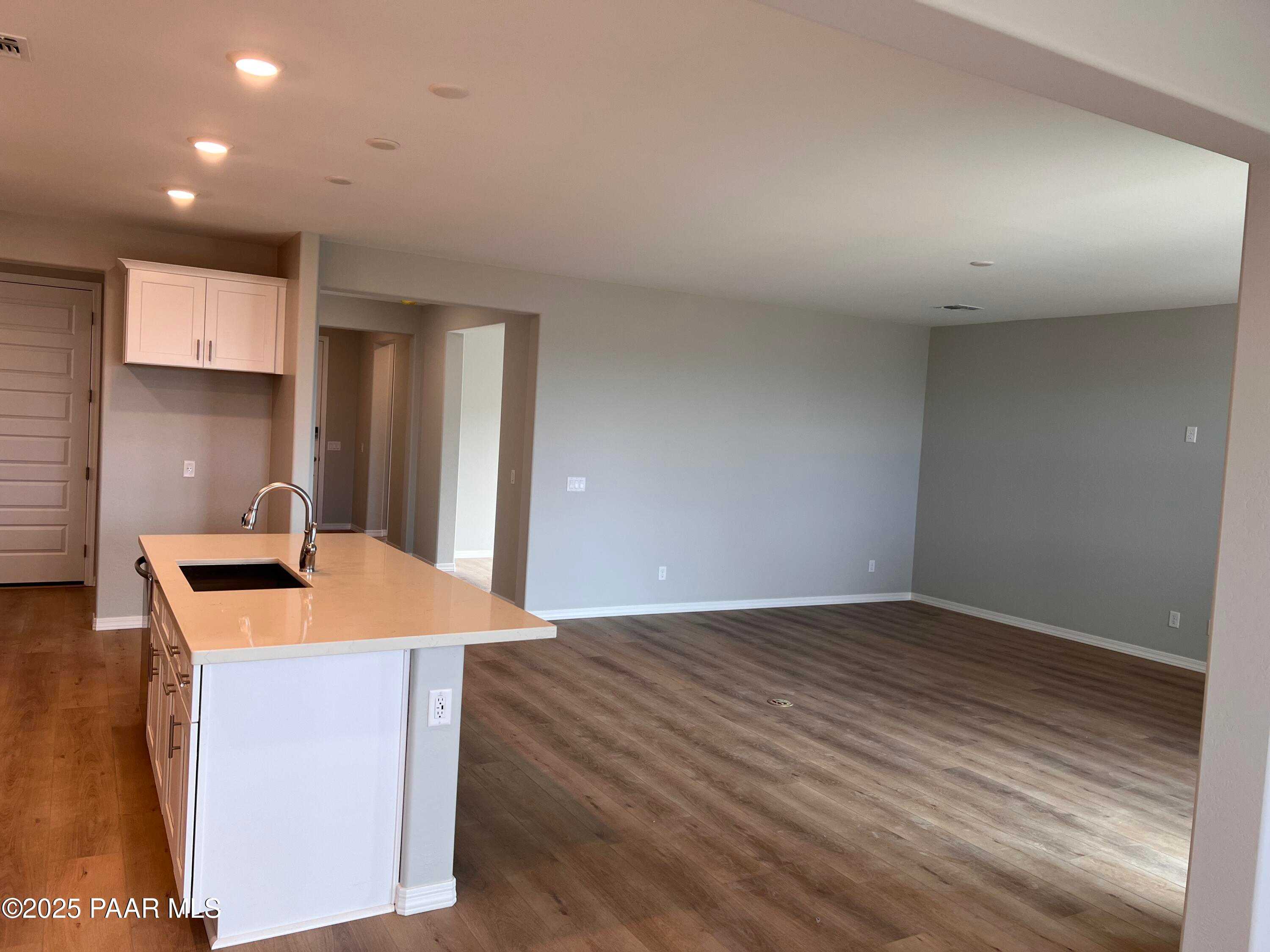 Open-concept kitchen with white cabinets, tan island sink, and wood flooring in Davidson Homes The Inspiration B, Prescott Valley, Arizona