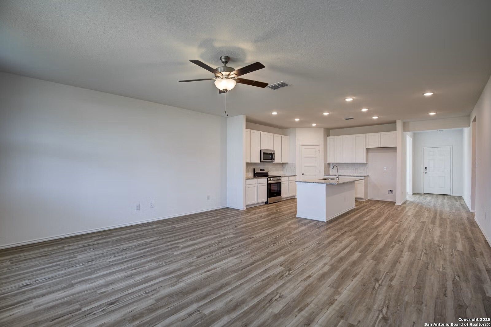 Open-concept kitchen with white shaker cabinets, large island, stainless appliances, and ceiling fan in Davidson Homes The Douglas B, Seguin, TX