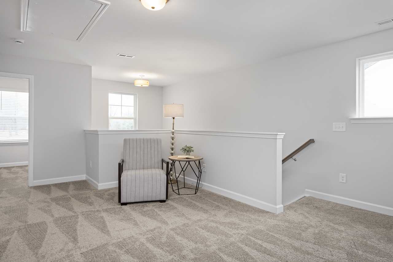 Spacious loft bonus room at Gregory Village in Lillington NC with gray walls, patterned carpet, striped armchair, side table, and balcony railing