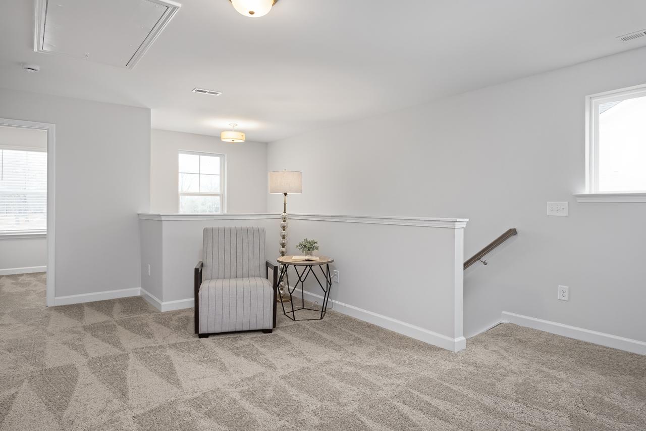 Spacious loft bonus room at Gregory Village in Lillington NC with gray walls, patterned carpet, striped armchair, side table, and balcony railing