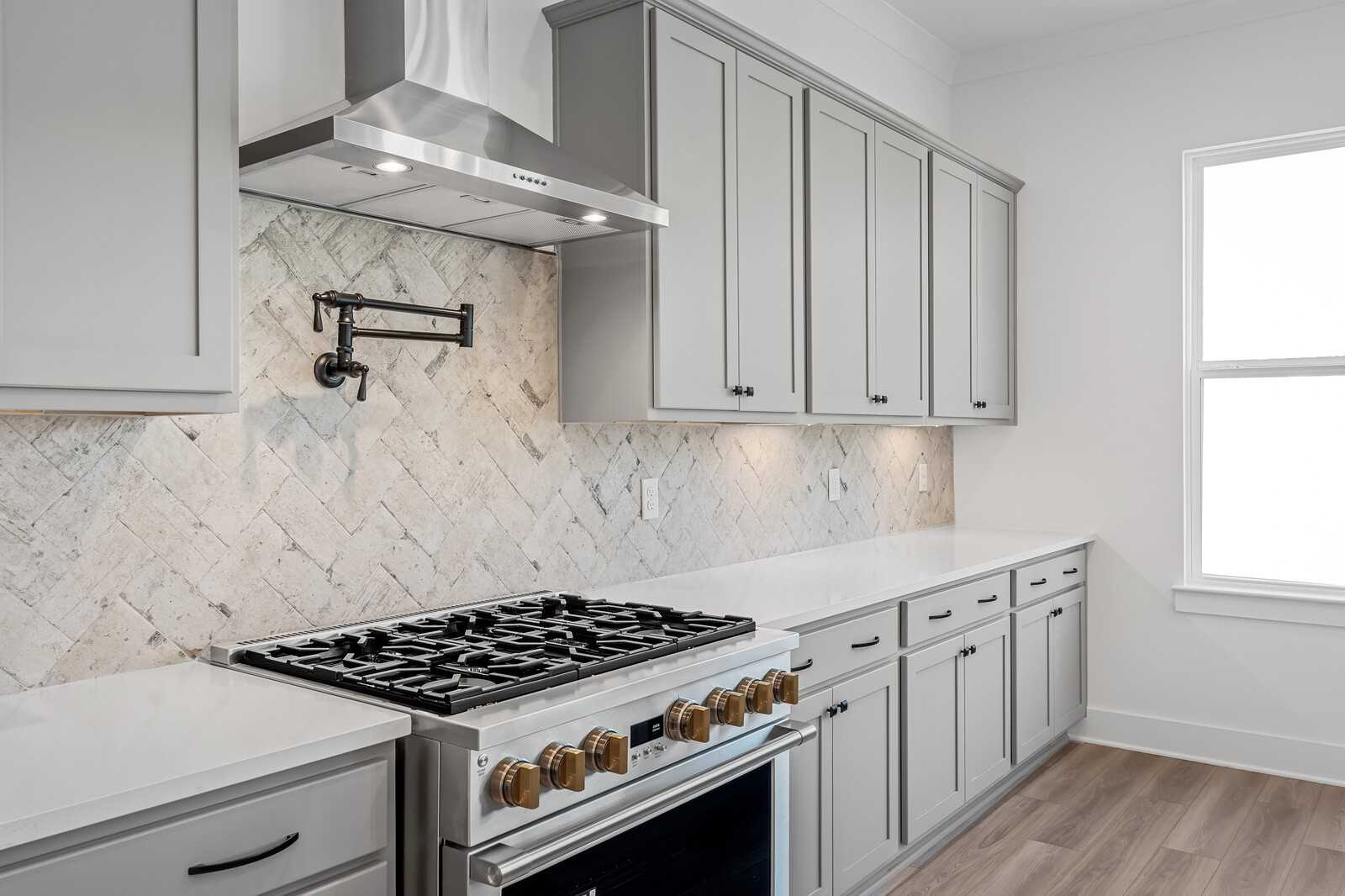 Modern kitchen featuring gray shaker cabinets, herringbone subway tile backsplash, and stainless gas range in The Alston A by Davidson Homes, Murfreesboro, TN