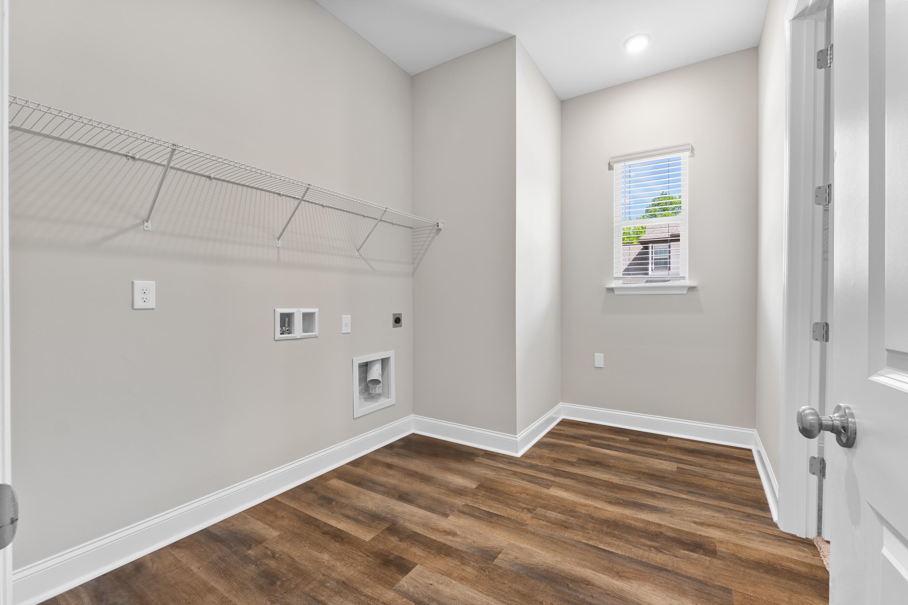 Spacious laundry room in The Arcadia B featuring wire shelving, washer-dryer hookups, window with blinds, and luxury vinyl plank flooring