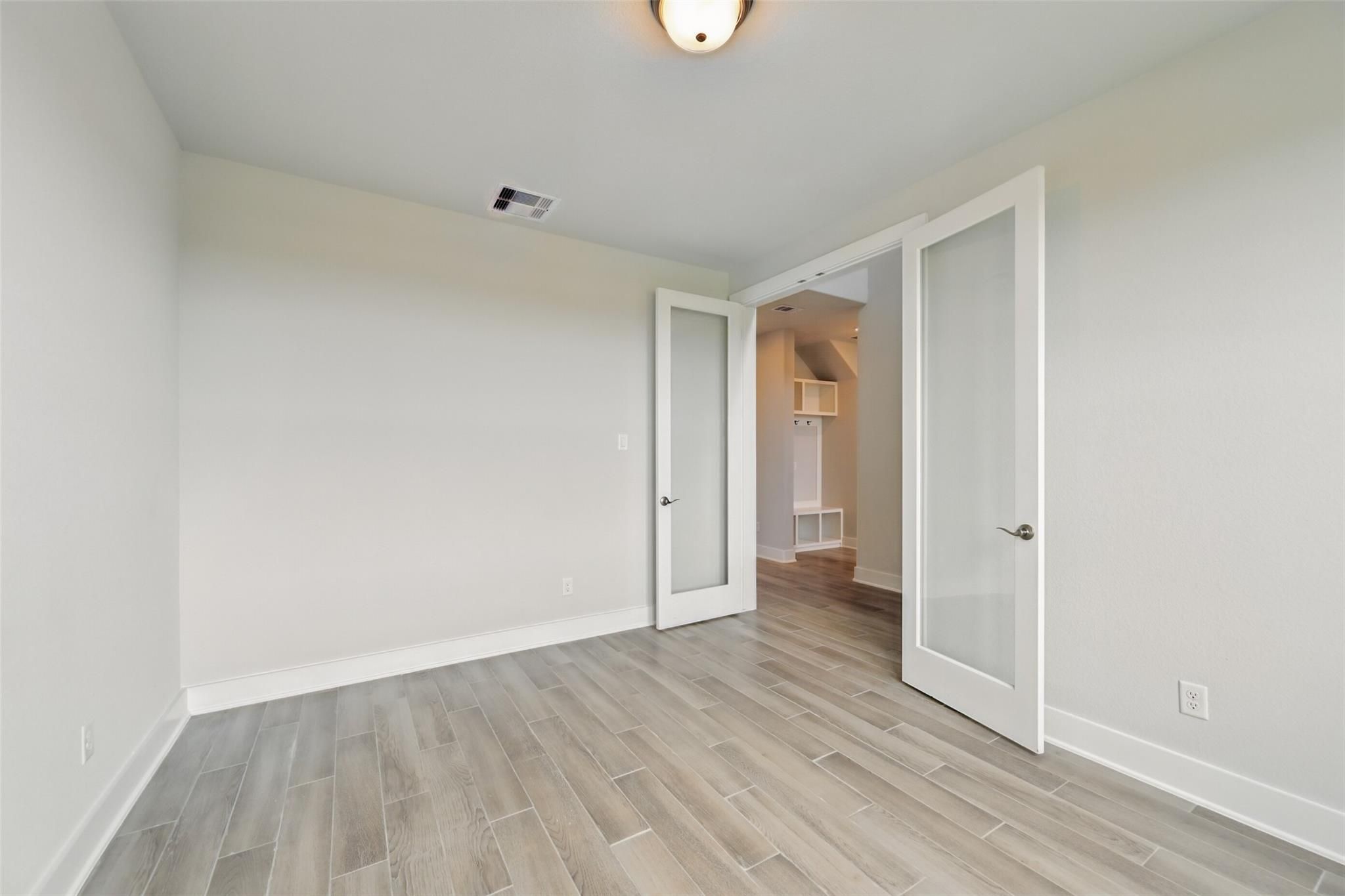 Bright bedroom with light wood floors, frosted glass doors to closet in Davidson Homes The Philip A, Lago Mar, Texas City