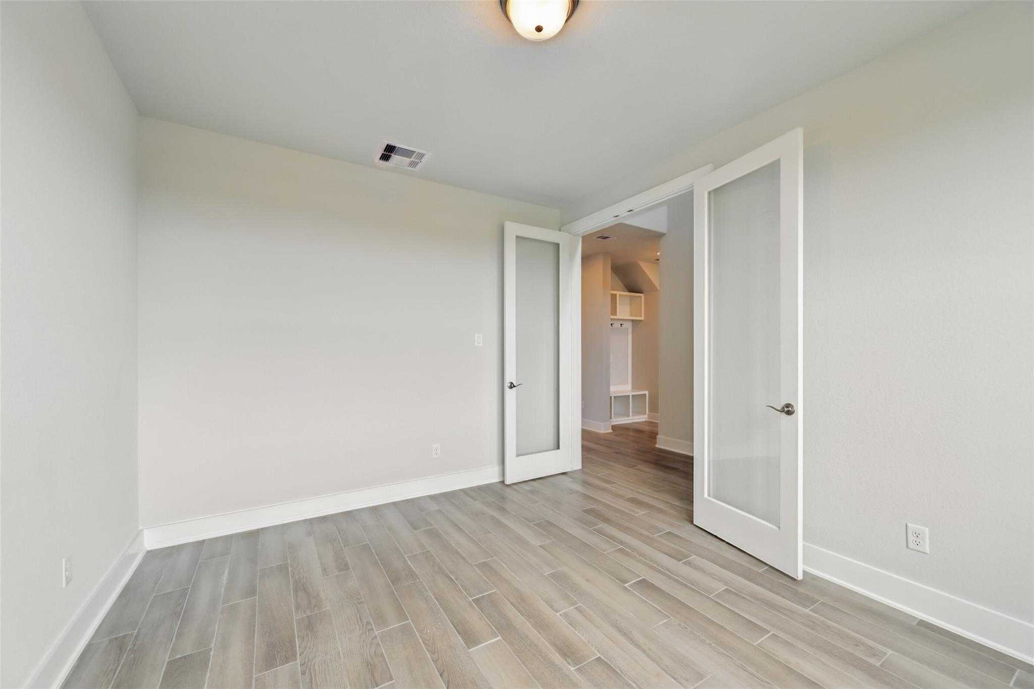 Bright bedroom with light wood floors, frosted glass doors to closet in Davidson Homes The Philip A, Lago Mar, Texas City