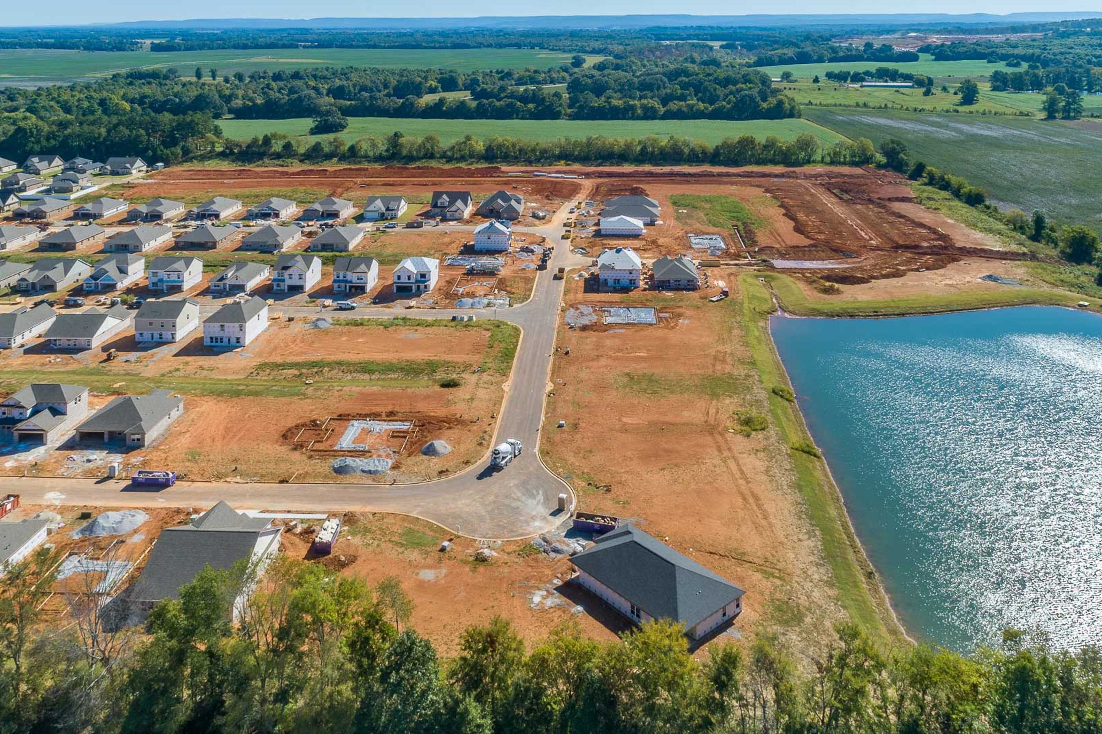 Aerial view of Ivy Hills neighborhood in Toney Alabama with new Davidson Homes under construction, dirt roads, and scenic pond