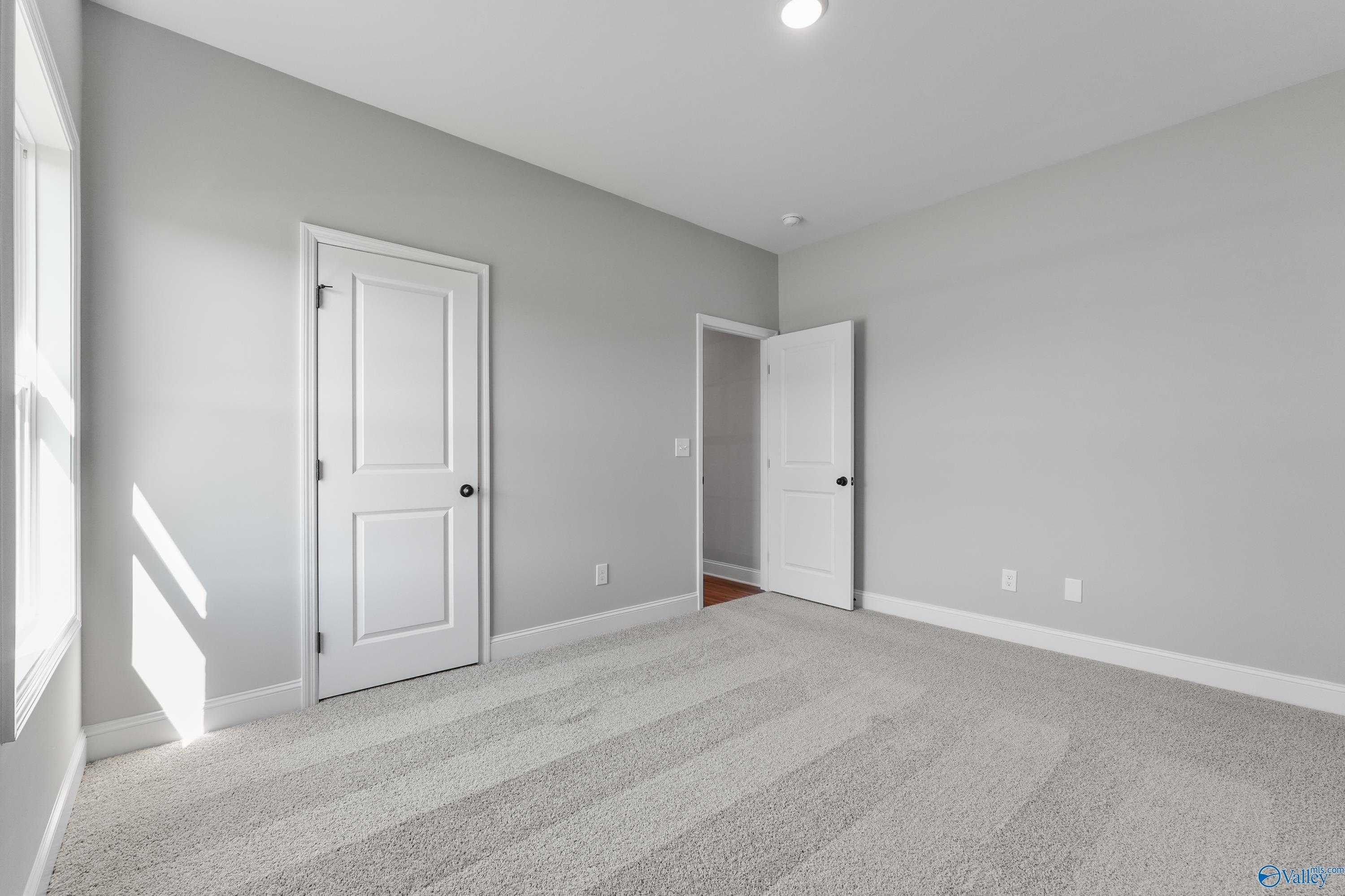 Spacious secondary bedroom with gray walls, white doors to closet and bath, plush carpeting in Davidson Homes The Daphne C, Hazel Green, AL