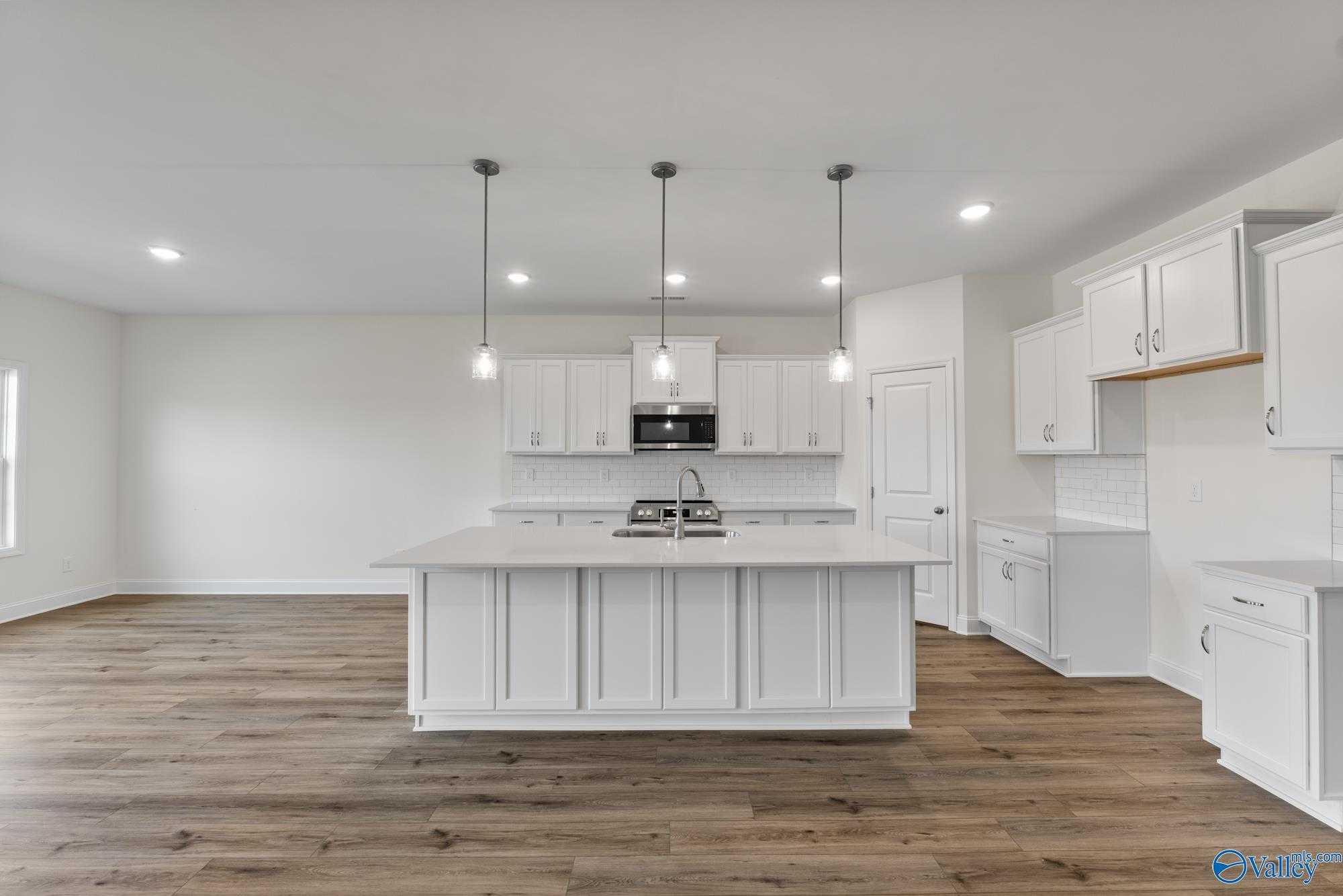 Modern white kitchen with spacious island, stainless steel appliances, pendant lights, and hardwood floors in Davidson Homes The Harrison, Meridianville, Alabama