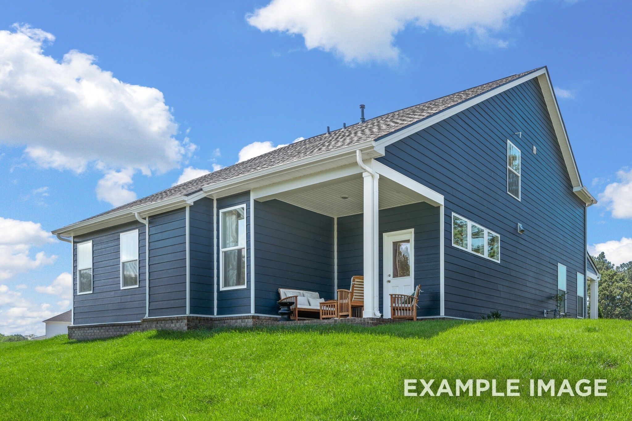 Two-story navy blue Davidson Homes The Ash A with covered front porch, white columns, and grassy hill view in Woods Crossing, Gallatin, Tennessee