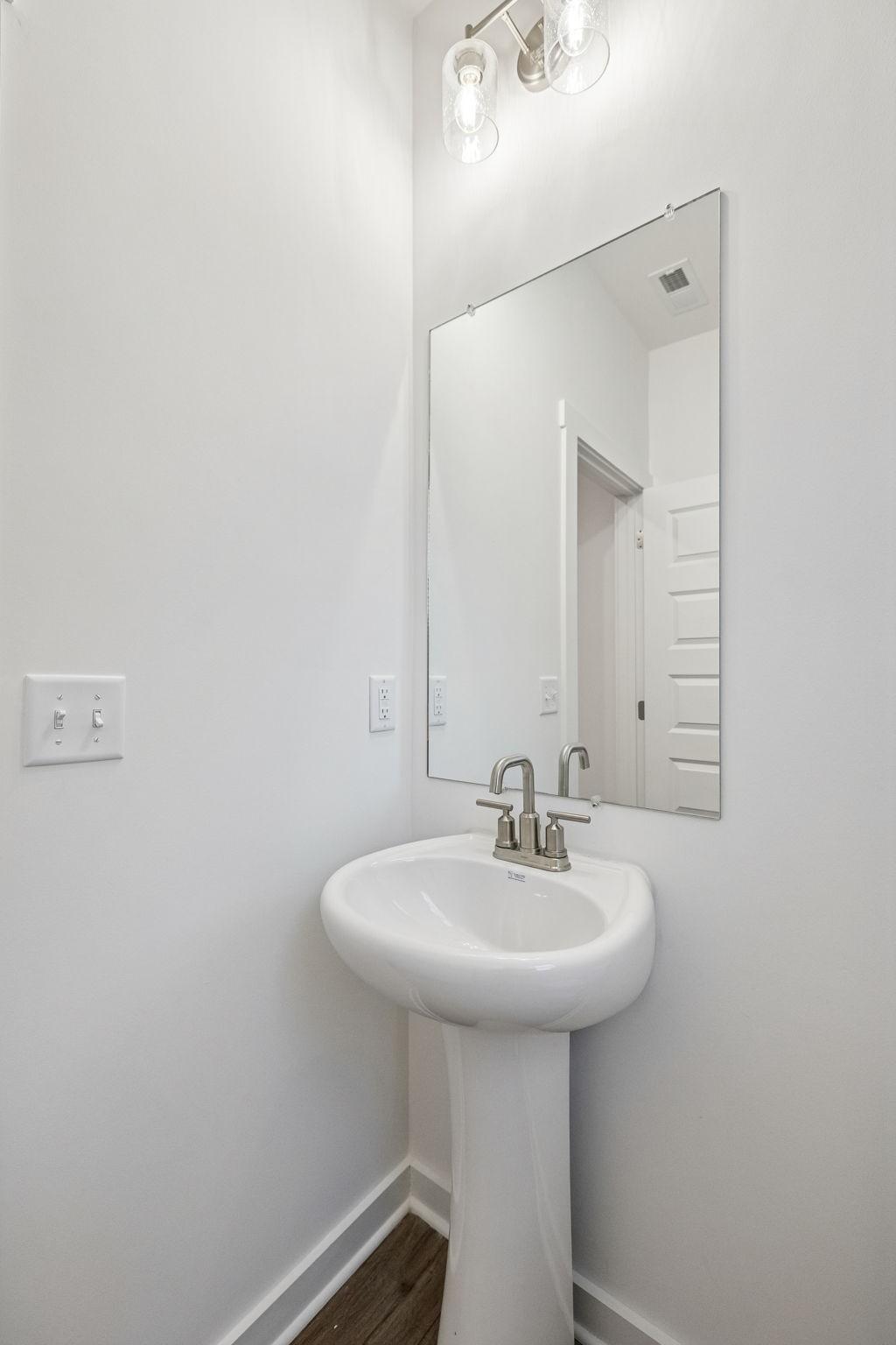 Elegant powder room with white pedestal sink, chrome faucet, and frameless mirror in Davidson Homes The Willow, Calista Farms
