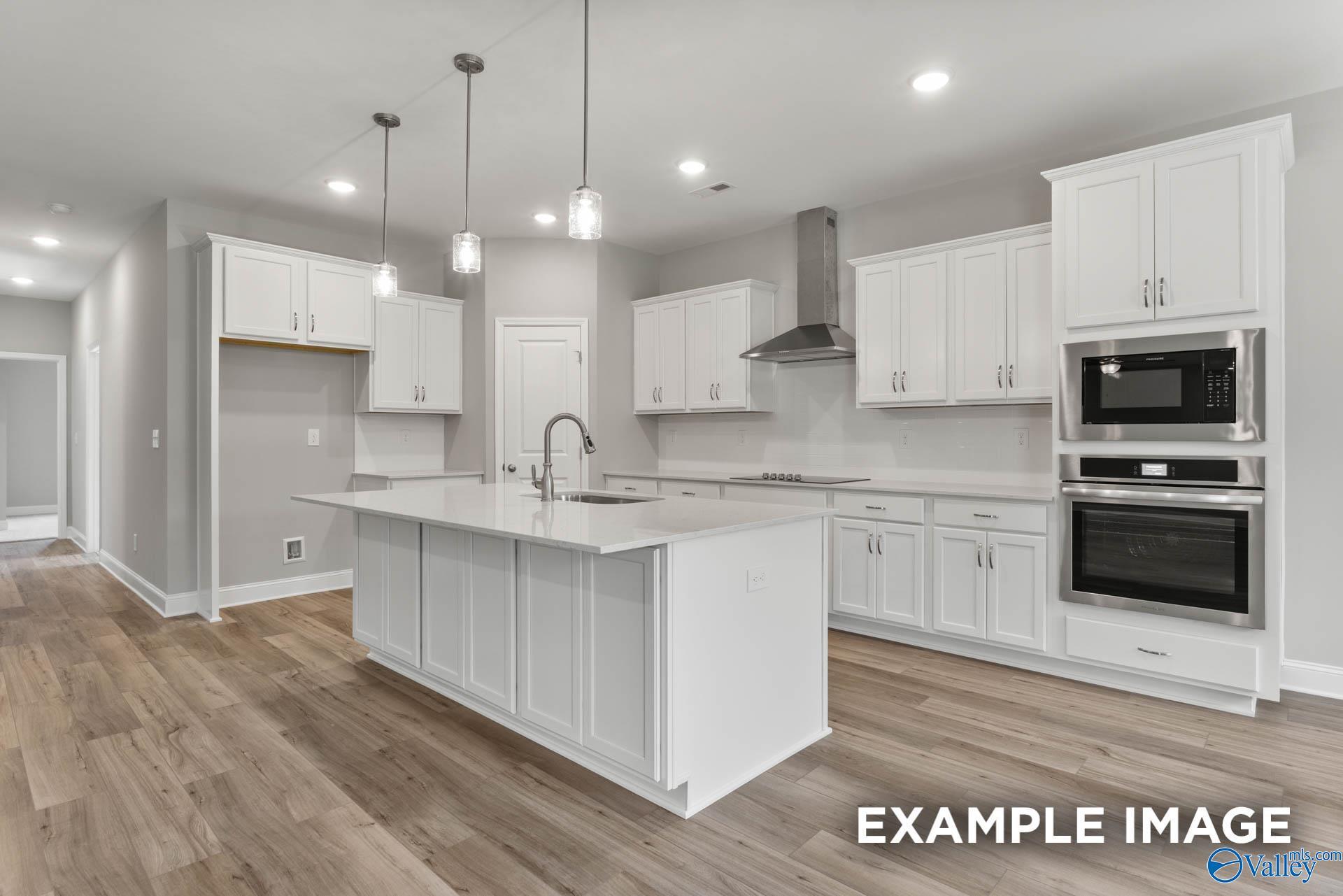 Modern white kitchen with large island sink, stainless double ovens, and pendant lights in Davidson Homes The Rockford with Bonus, Madison Alabama