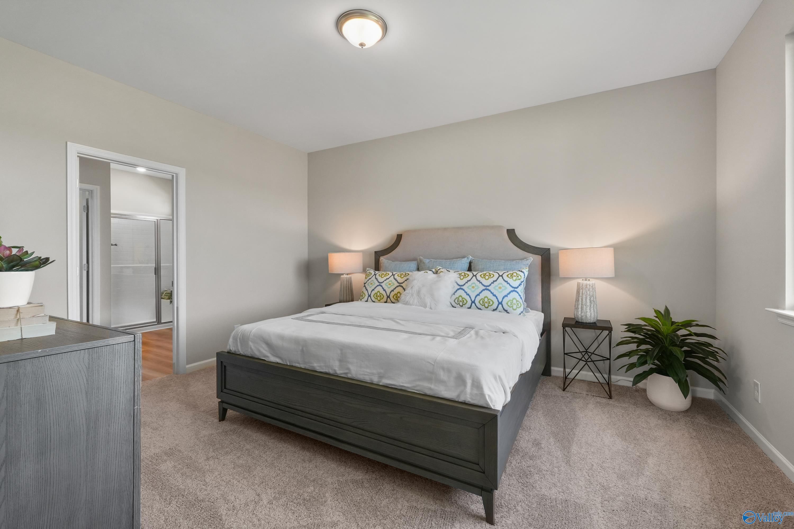 Elegant master bedroom with king bed, neutral walls, en-suite bath door, and plants in Evermore Homes The Malibu, Madison, Alabama