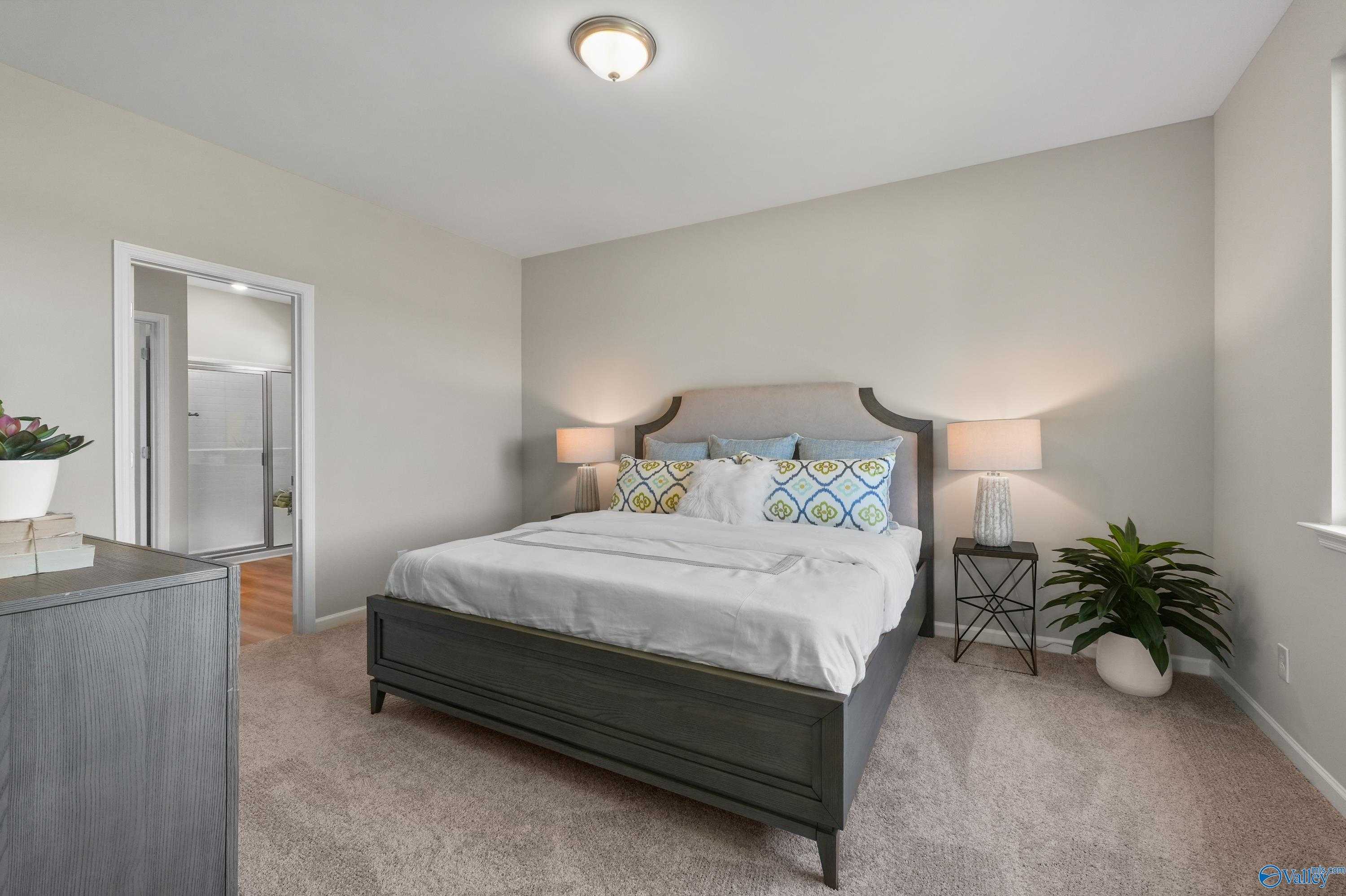 Elegant master bedroom with king bed, neutral walls, en-suite bath door, and plants in Evermore Homes The Malibu, Madison, Alabama