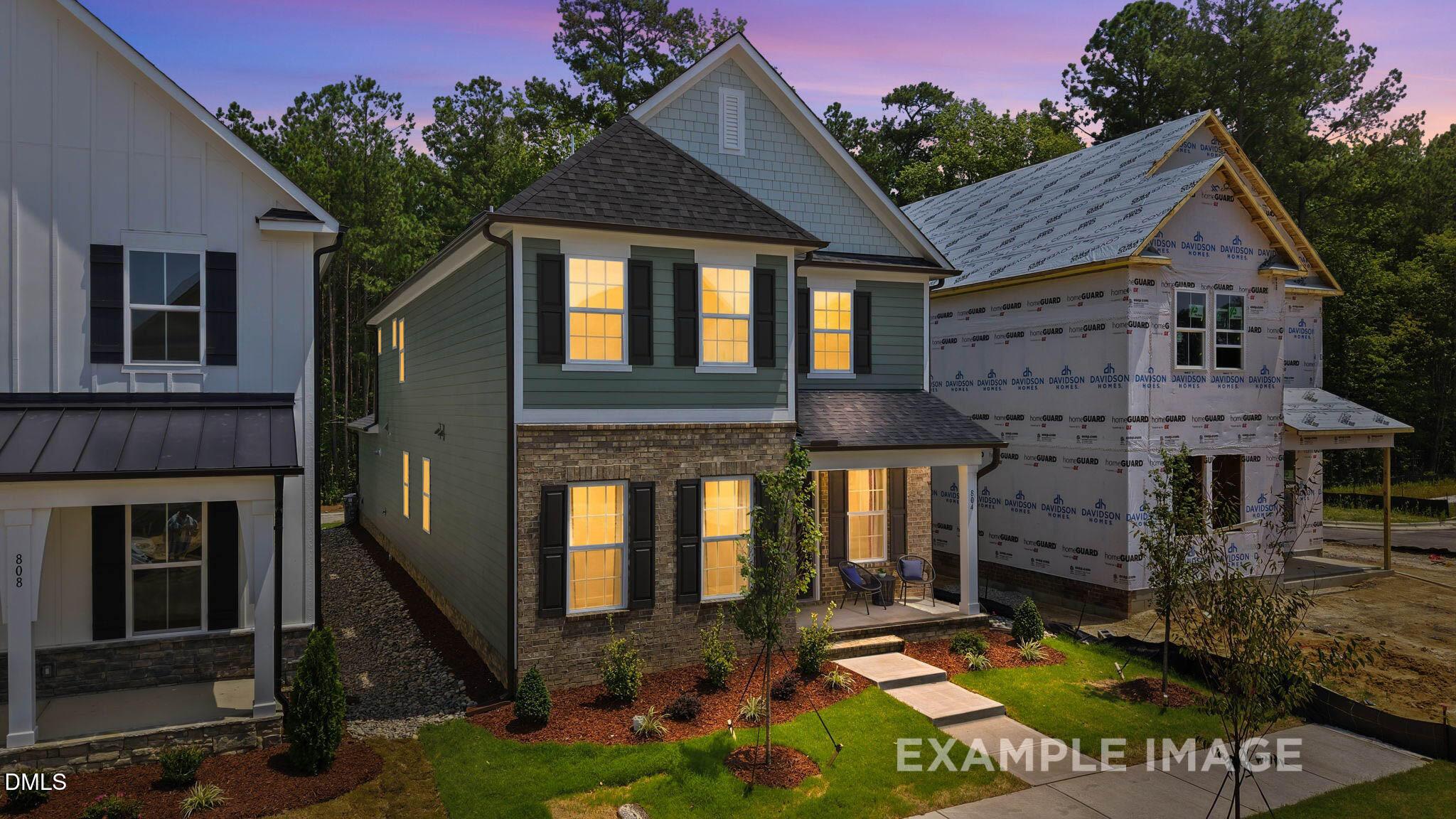 Two-story brick and sage green home with covered front porch at dusk in Forestville Yard, Knightdale, NC by Davidson Homes