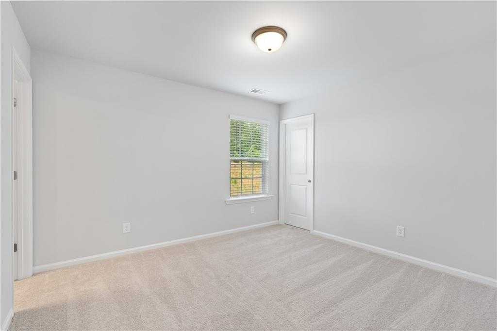 Bright empty bedroom with white walls, beige carpet, window blinds, and ceiling light in Davidson Homes The Hickory B, Winder, GA