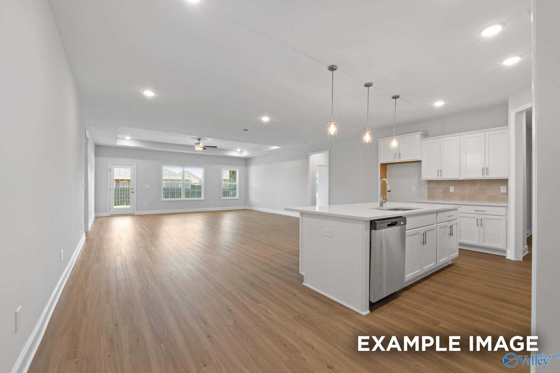 Open-concept kitchen and living space with white island, hardwood floors, large windows, and stainless appliances in Davidson Homes The Lanier, Meridianville, Alabama
