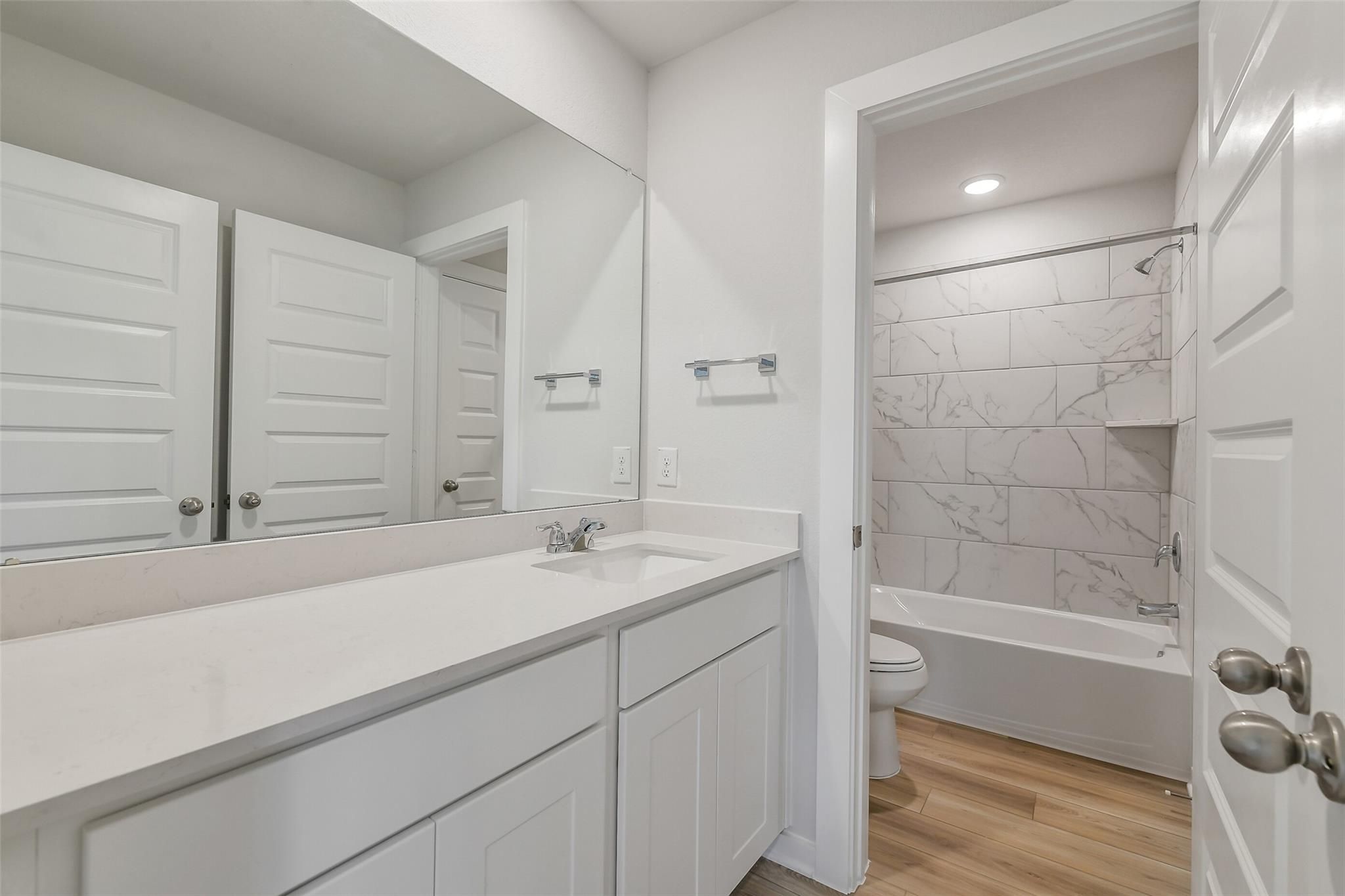 Modern bathroom with white quartz vanity, large mirror, and marble-tile tub-shower combo in Davidson Homes San Marcos E, Conroe TX