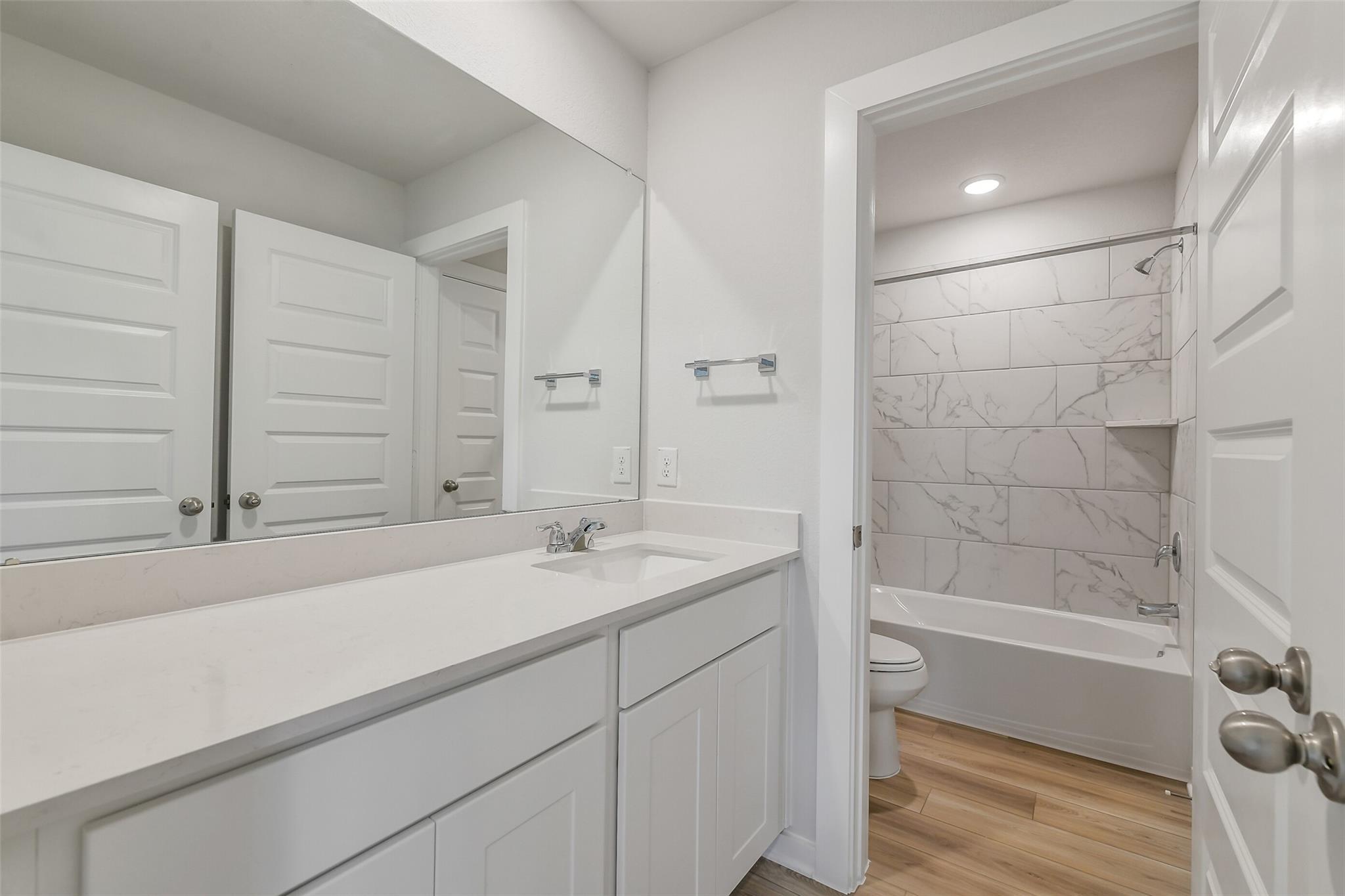 Modern bathroom with white quartz vanity, large mirror, and marble-tile tub-shower combo in Davidson Homes San Marcos E, Conroe TX