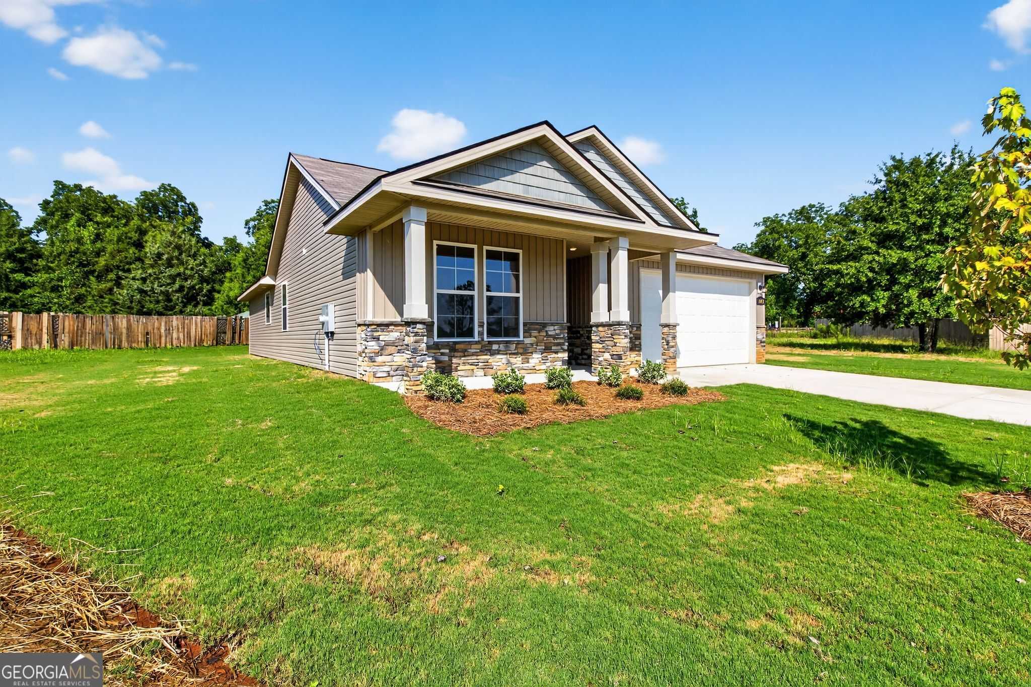 Charming tan single-story 4-bedroom home with gabled roof, covered porch, two-car garage, and landscaped yard in Ivy Glen, Perry, Georgia - Evermore Homes The Luna