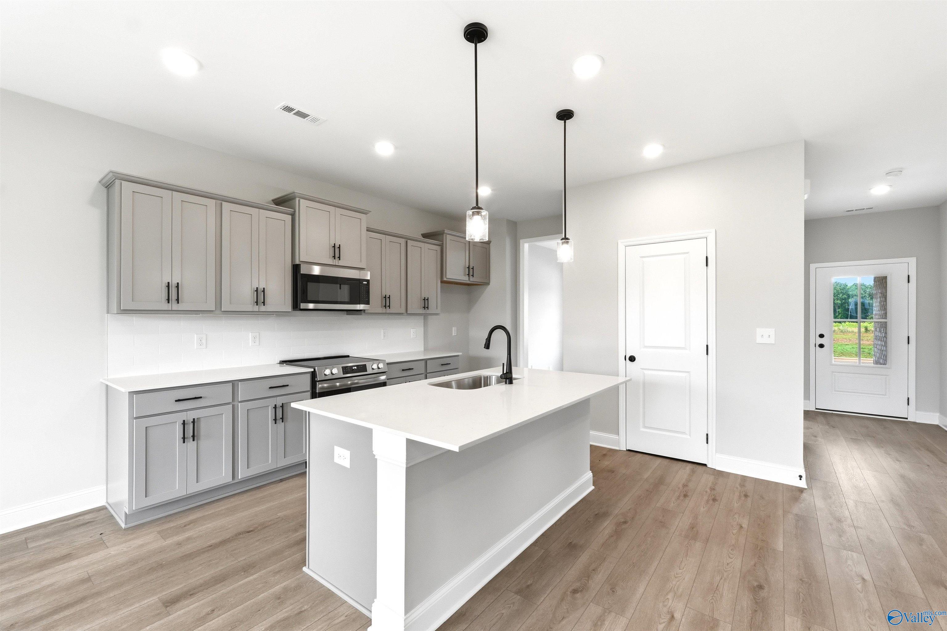 Modern kitchen with gray cabinets, quartz island, and pendant lighting in The Shelby A floor plan, Wood Trail, Toney, AL.