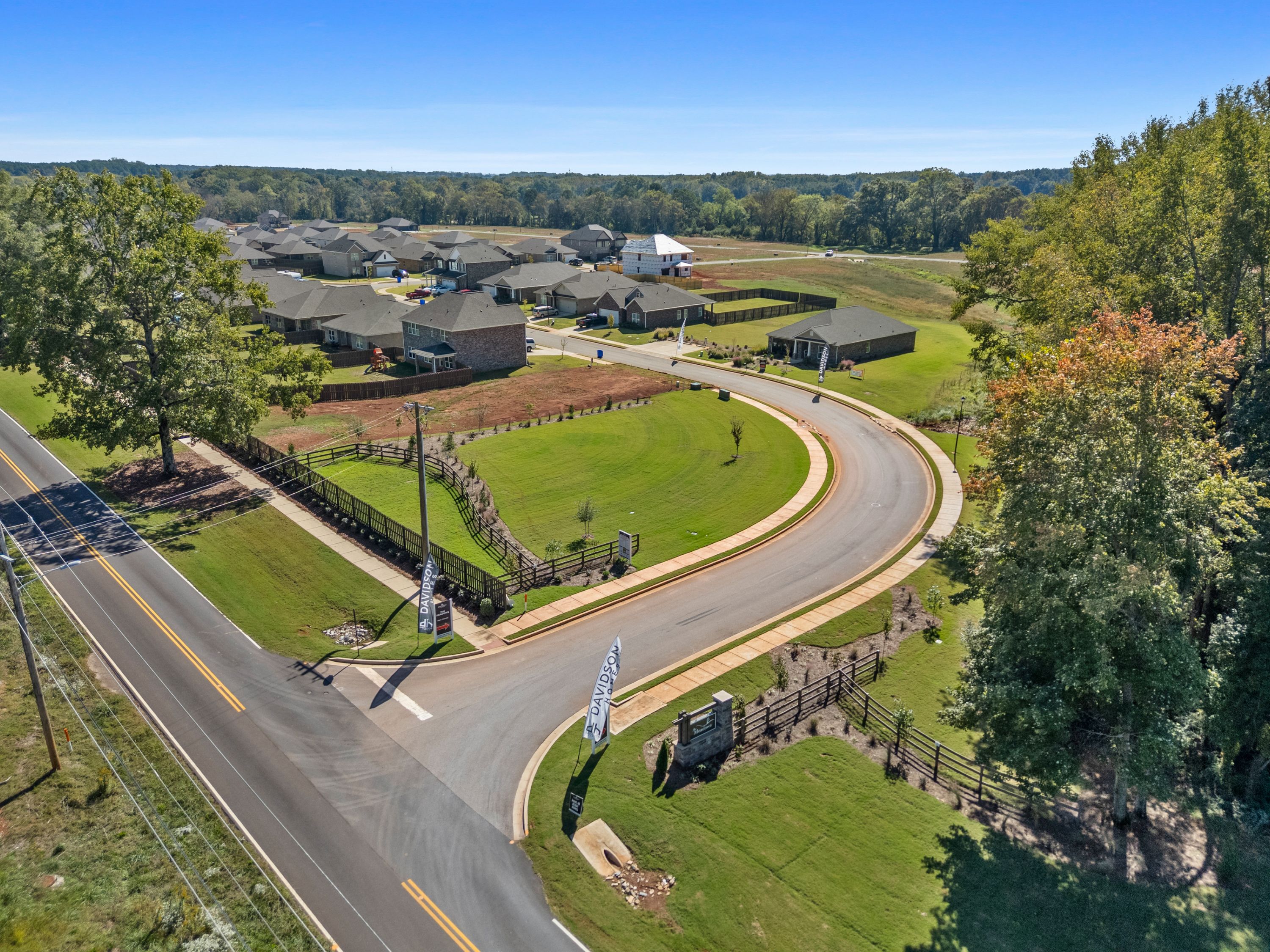 Entrance to The Meadows in Athens Alabama by Davidson Homes with curved road, new homes, lush lawns, and trees
