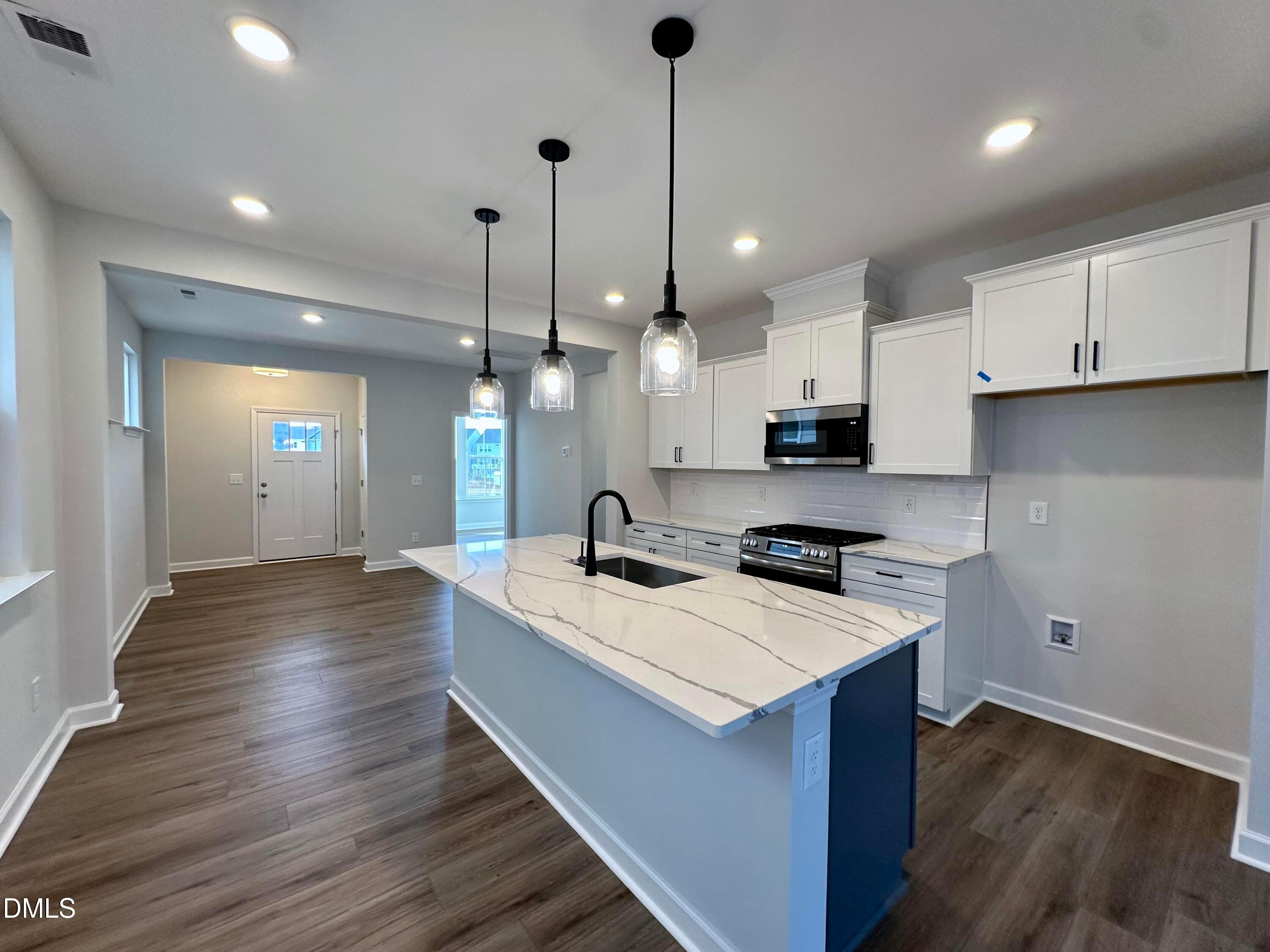 Modern kitchen featuring white quartz island, stainless steel appliances, and pendant lights in Davidson Homes The Alexander B, Knightdale, NC