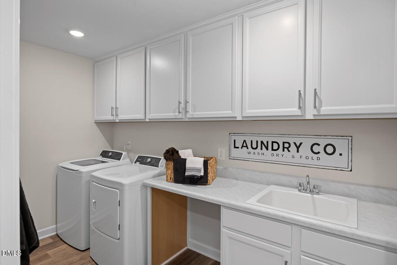 Modern laundry room with white cabinets, washer, dryer, utility sink, and "LAUNDRY CO." sign in Davidson Homes The Hickory II C, Zebulon, NC