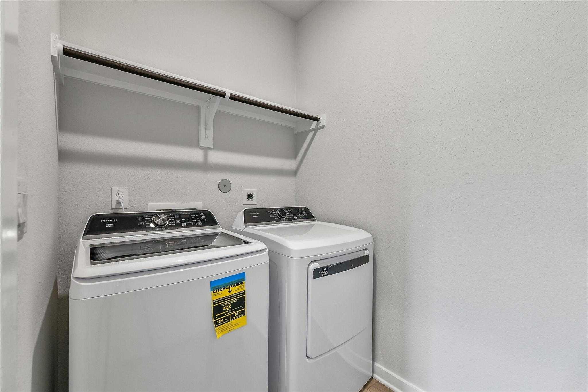 Spacious laundry room with white front-load washer, dryer and built-in shelves in Davidson Homes The Colorado G, Magnolia, Texas