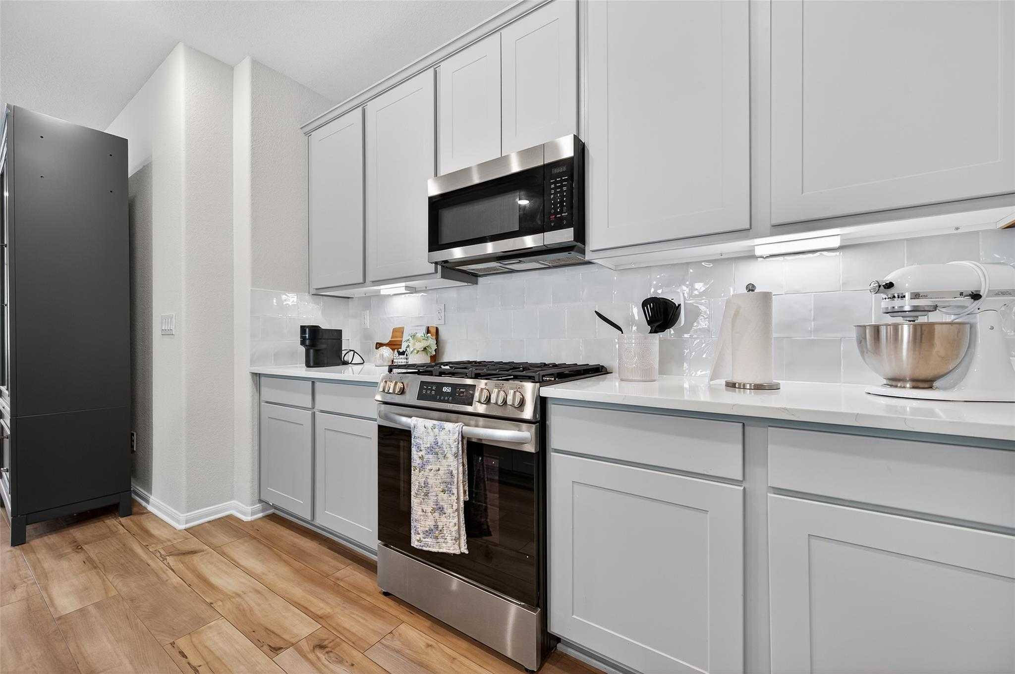 Modern white shaker kitchen with stainless steel appliances, quartz counters, and subway tile backsplash in Brazos E home, Magnolia, TX