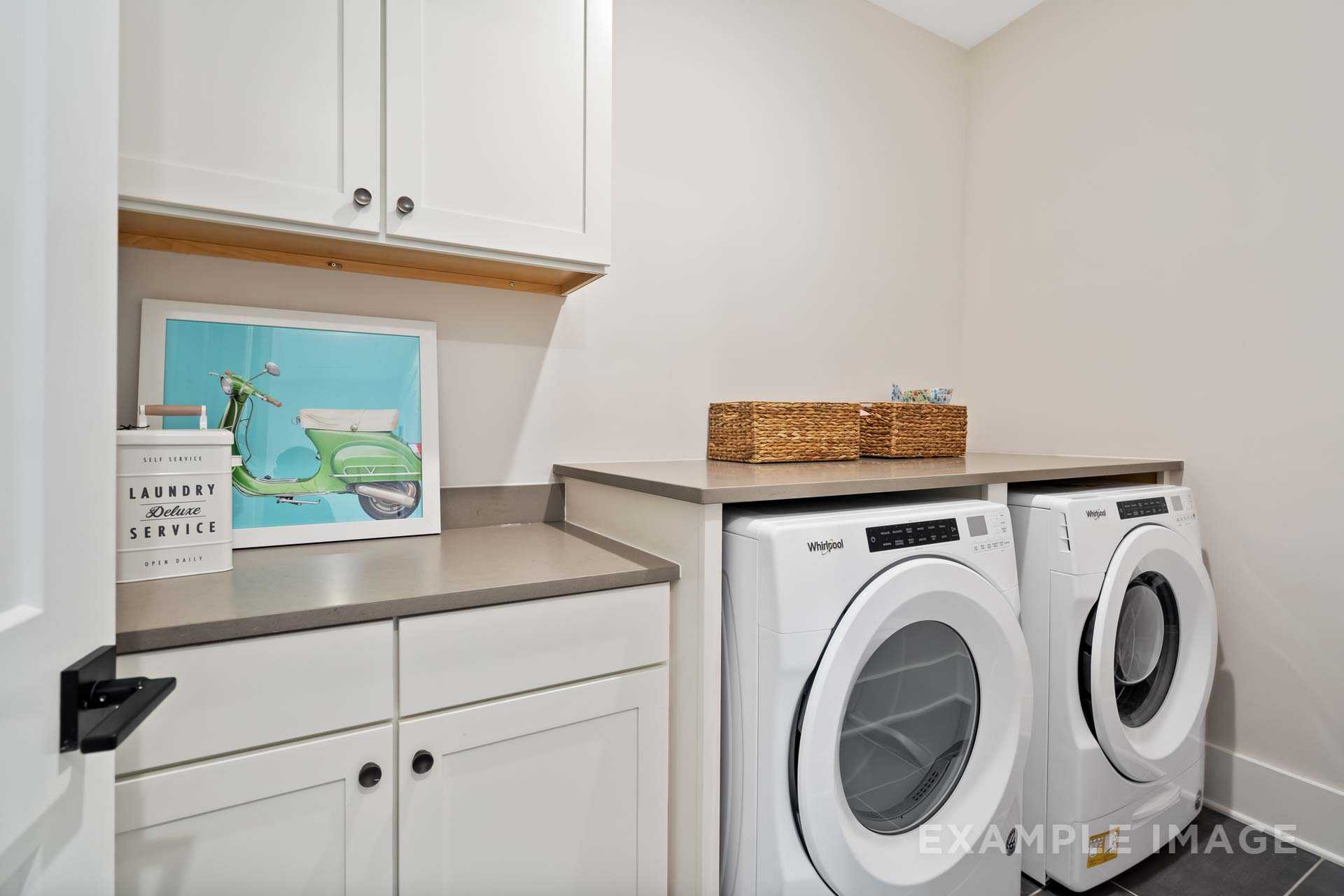Modern laundry room at Manor Estates in Marietta GA featuring white shaker cabinets, Whirlpool washer dryer, and woven basket storage
