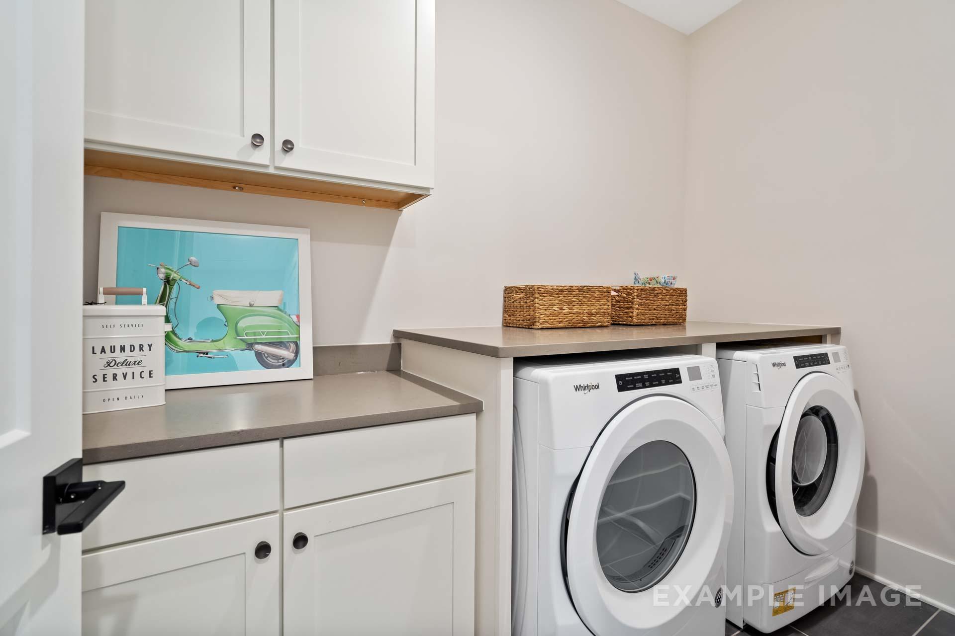 Modern laundry room at Manor Estates in Marietta GA featuring white shaker cabinets, Whirlpool washer dryer, and woven basket storage
