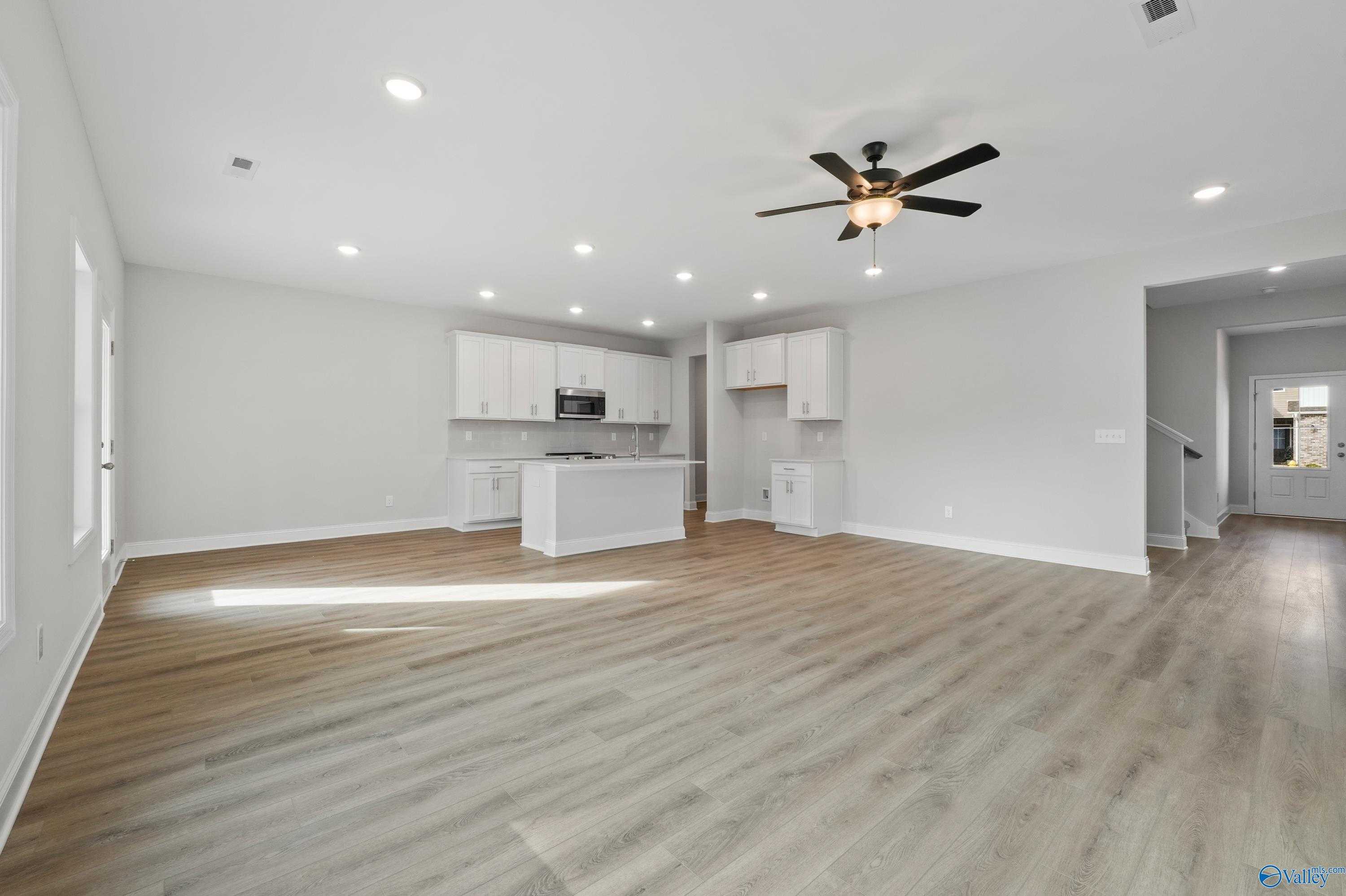 Open-concept kitchen with white shaker cabinets, large island, stainless appliances, and hardwood floors in The Camden by Davidson Homes, Huntsville AL
