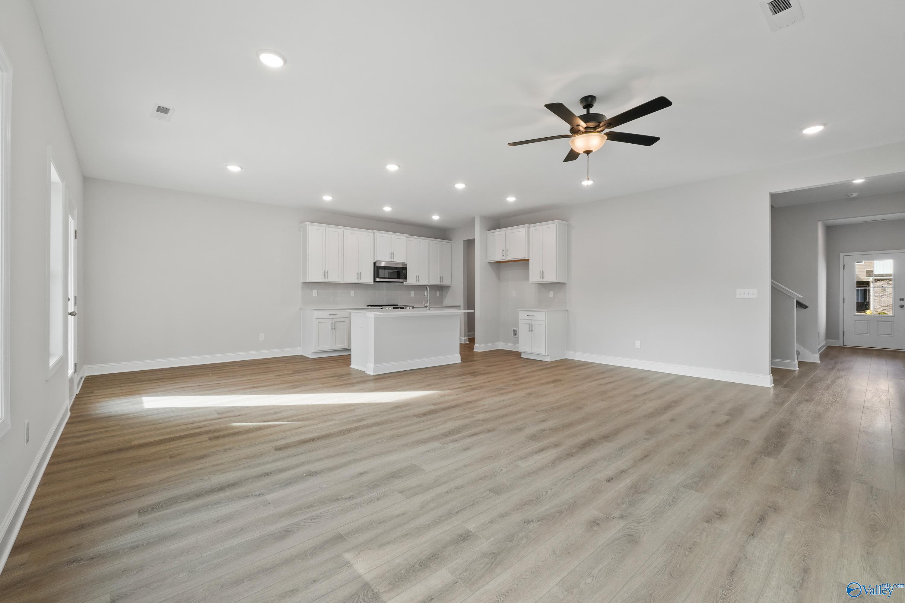 Open-concept kitchen with white cabinets, stainless appliances, island, and ceiling fans in Davidson Homes The Camden, Huntsville, AL
