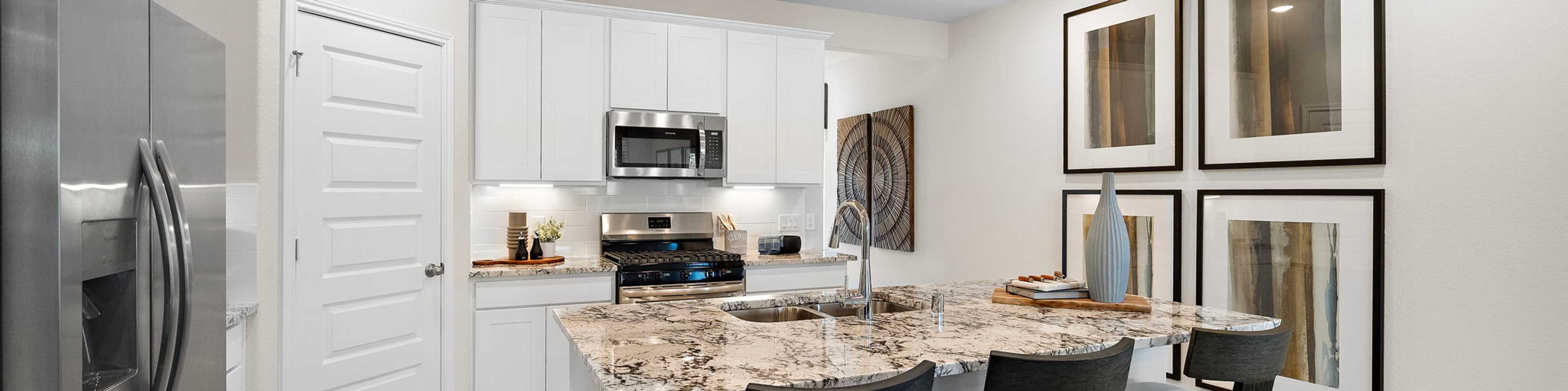 Modern kitchen at Lakes at Black Oak in Magnolia TX with white cabinets, granite island, black bar stools, and stainless appliances