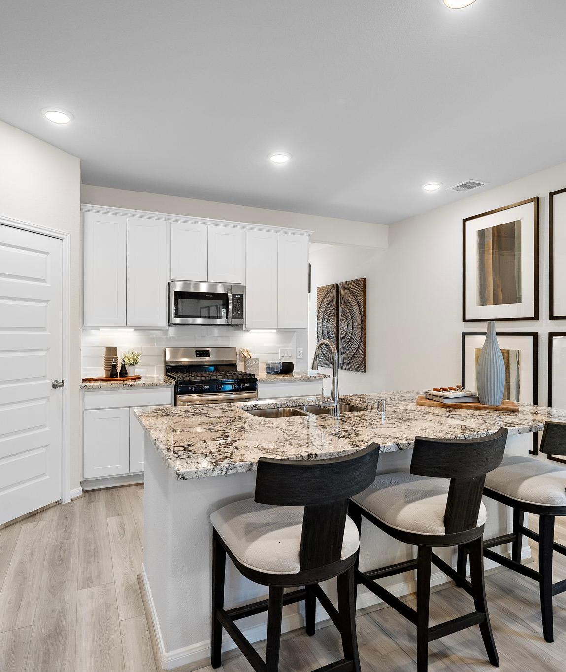 Modern kitchen at Lakes at Black Oak in Magnolia TX with white cabinets, granite island, black bar stools, and stainless appliances