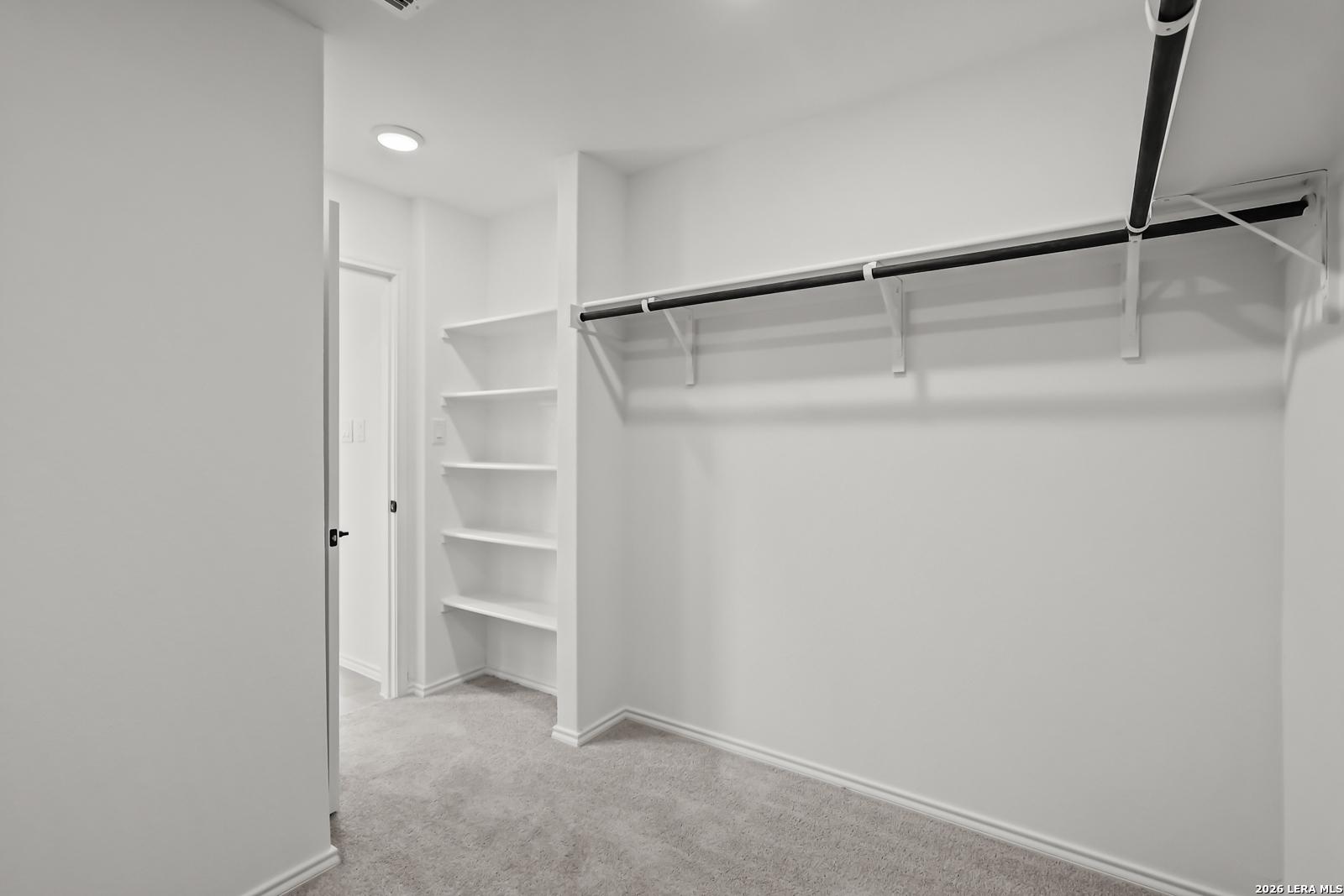 Walk-in closet with built-in shelving and hanging rod in The Florence B floor plan at Meadows at Oak Creek, San Antonio.