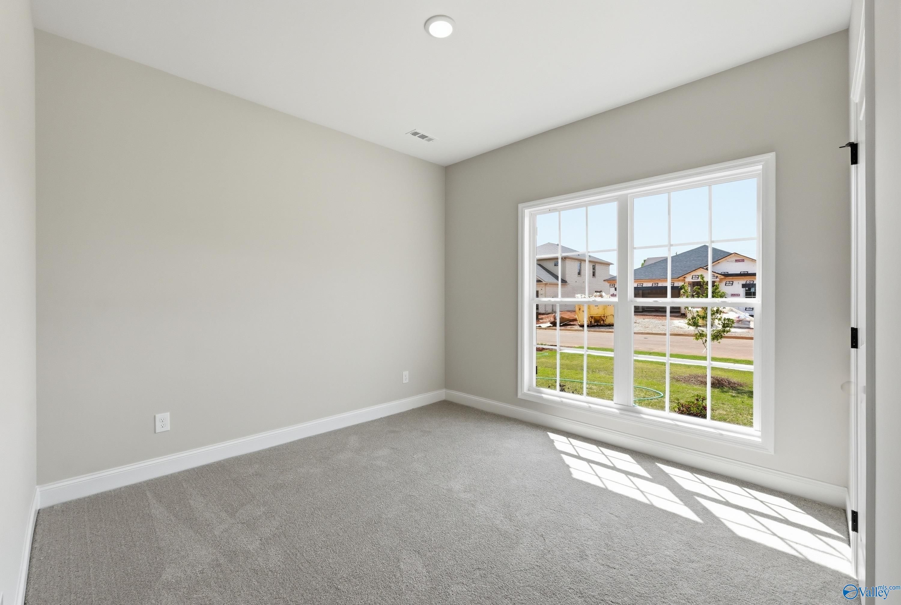 Bright empty bedroom with gray carpet, light walls, and large window overlooking Lynn Meadows in Meridianville, Alabama