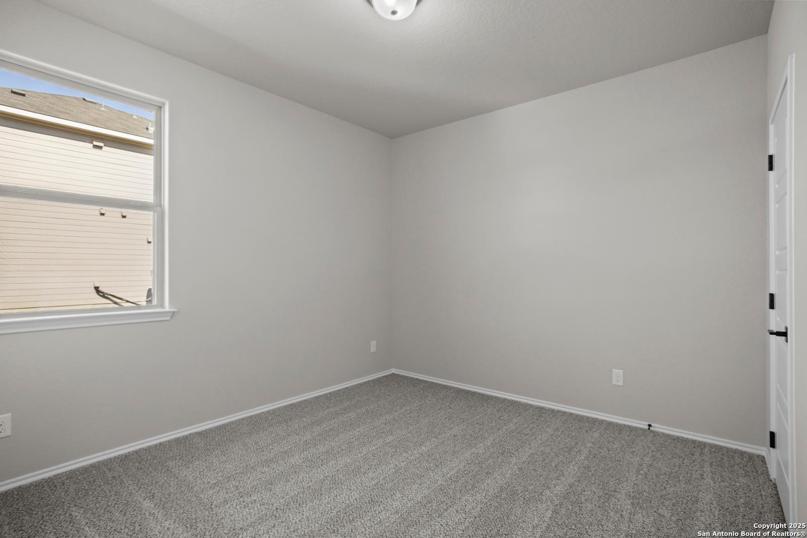 Bright secondary bedroom with light gray walls, beige carpet, large window in The Daphne H by Davidson Homes, Seguin, Texas