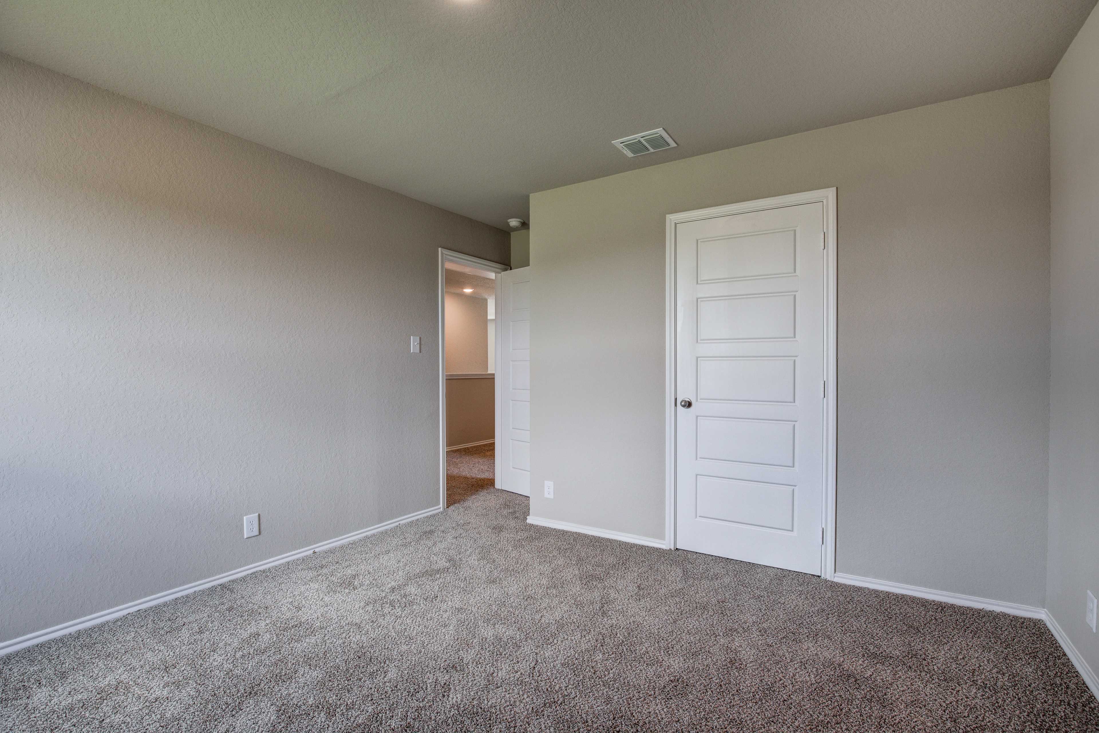 Spacious upstairs bedroom in The Murray Davidson Homes design with neutral beige walls, carpeted floor, and white door to adjacent bath