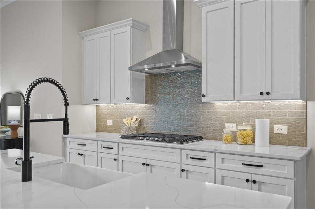 Elegant white shaker kitchen with quartz counters, stainless range hood, mosaic backsplash, and black faucet in Davidson Homes The Seaside B, Woodstock, GA
