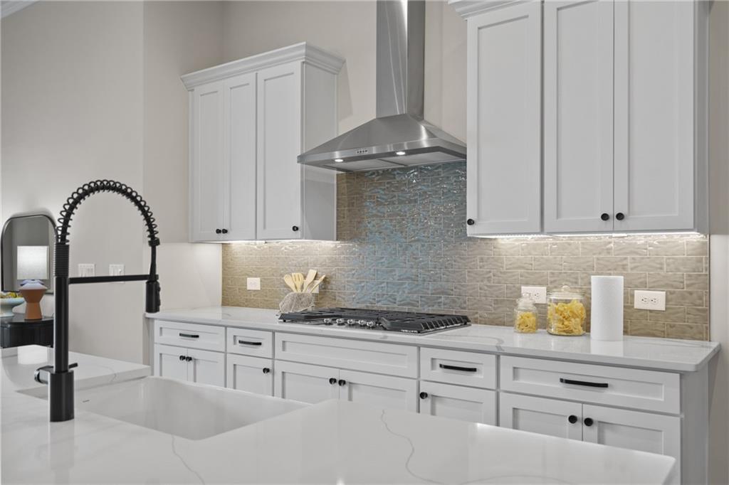 Elegant white shaker kitchen with quartz counters, stainless range hood, mosaic backsplash, and black faucet in Davidson Homes The Seaside B, Woodstock, GA