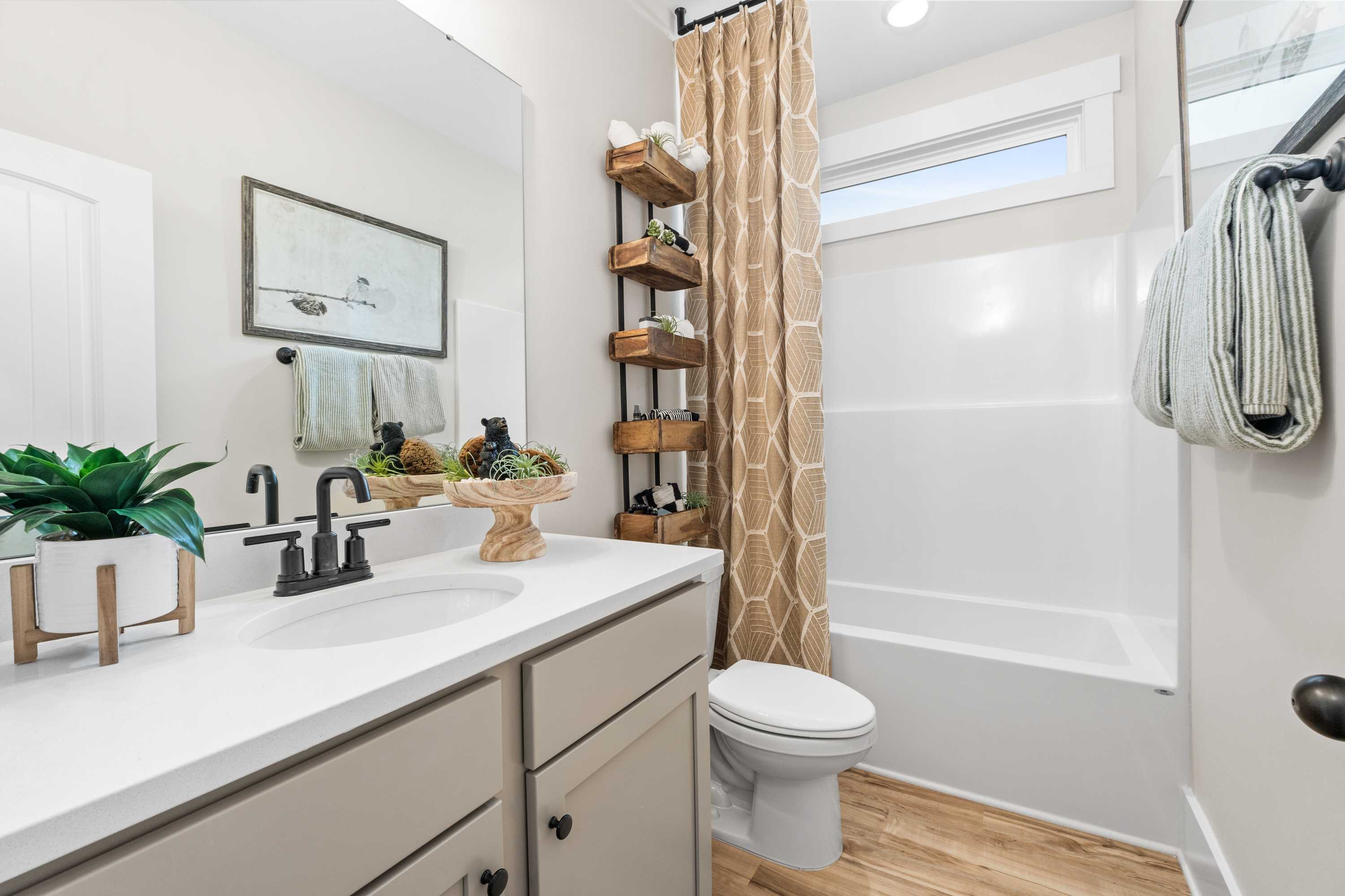 Modern bathroom at Spragins Cove in Huntsville AL with gray vanity, wooden shelves, potted plants, and subway tile shower