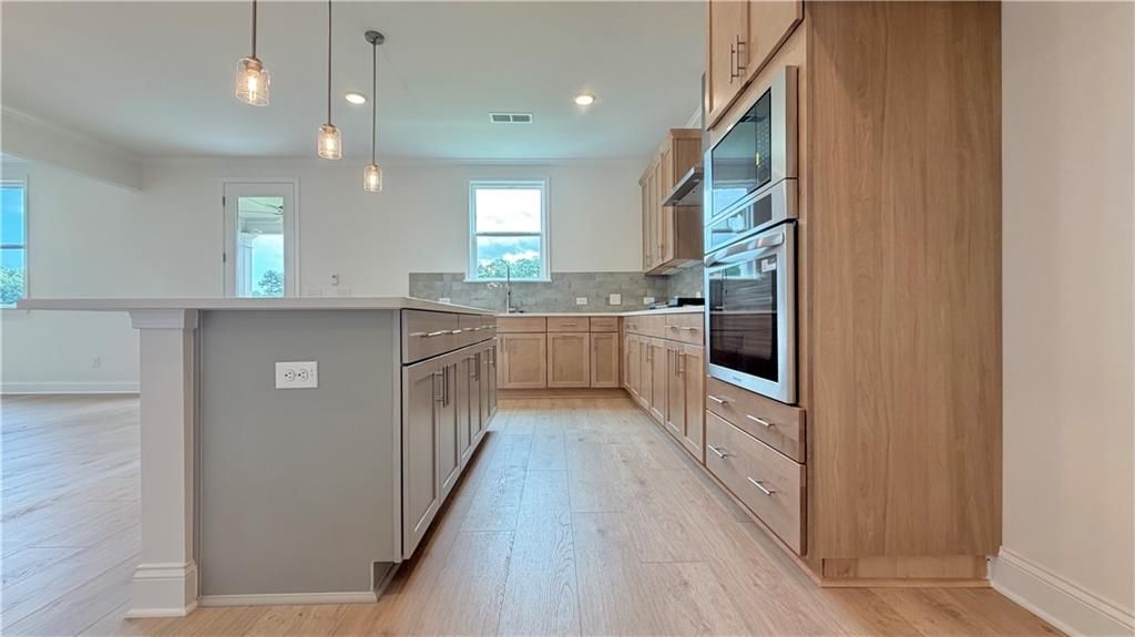 Modern kitchen with light wood cabinetry, center island, and stainless steel wall oven in Hickory C home in Hoschton, GA.