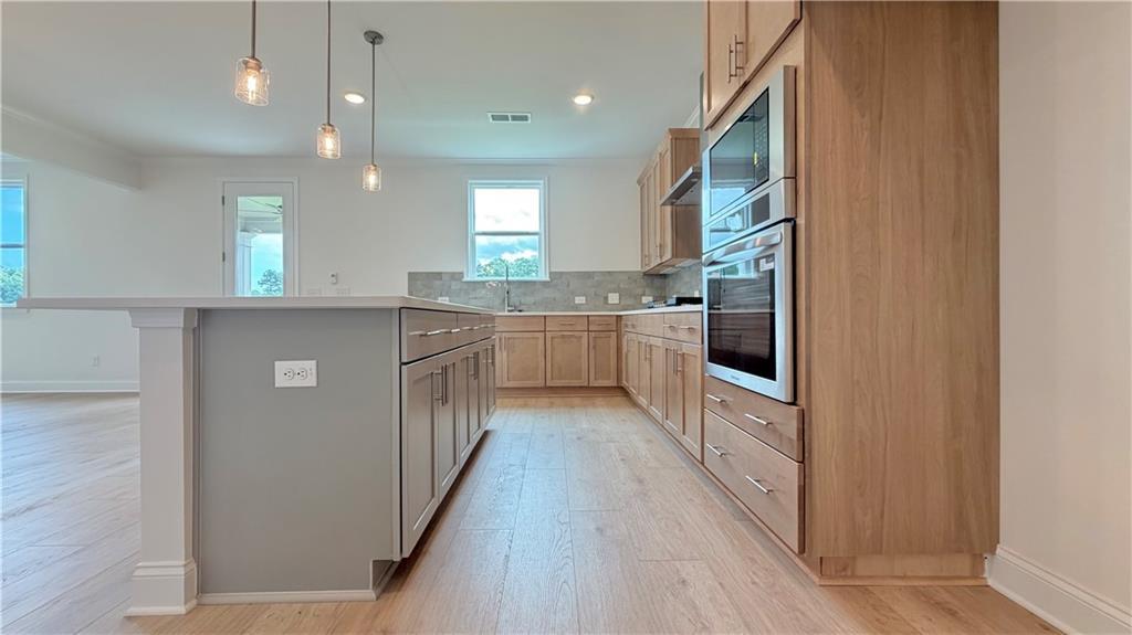 Modern kitchen with light wood cabinetry, center island, and stainless steel wall oven in Hickory C home in Hoschton, GA.