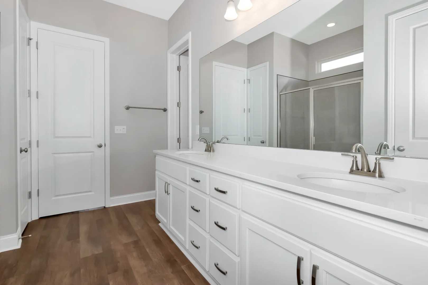 Spacious master bathroom in The Arcadia M with double white vanity, frameless glass shower, and light wood floors