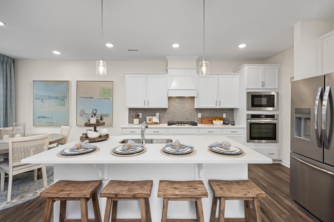 Open-concept kitchen at Gregory Village Townhomes in Lillington NC with white cabinets, large island, stainless appliances, and hardwood floors