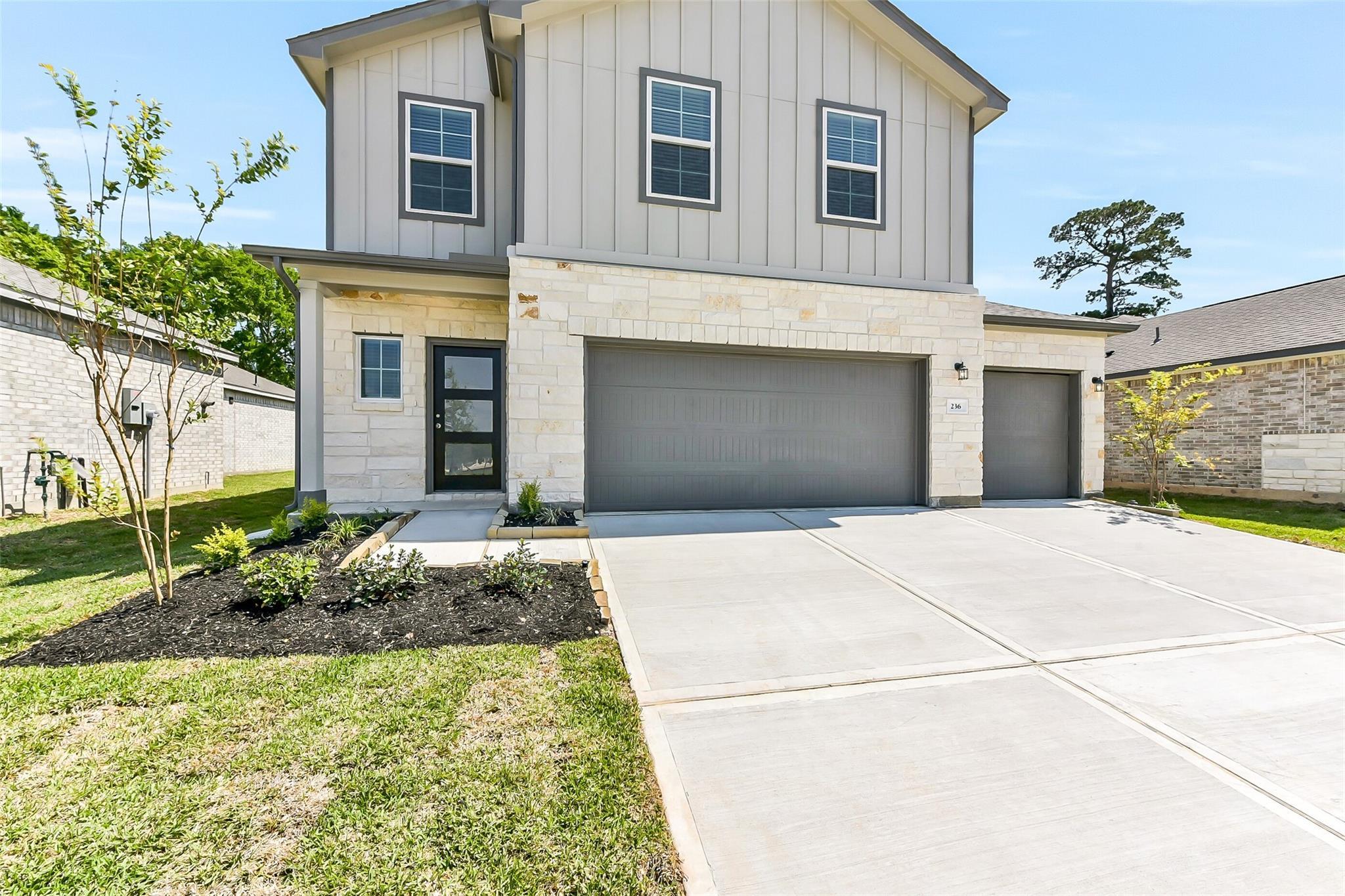 Modern two-story 5-bedroom home exterior with 3-car garage, stone facade, and landscaped yard in Windmill Estates, Magnolia, Texas