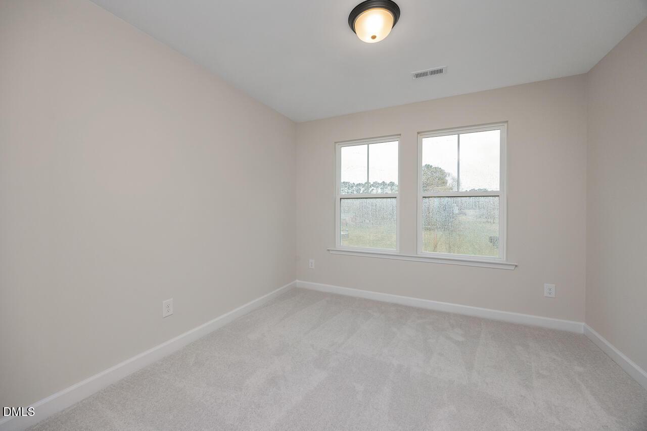 Bright bedroom with beige walls, neutral carpet, dual windows overlooking woods in Davidson Homes The Mitchell, Knightdale NC