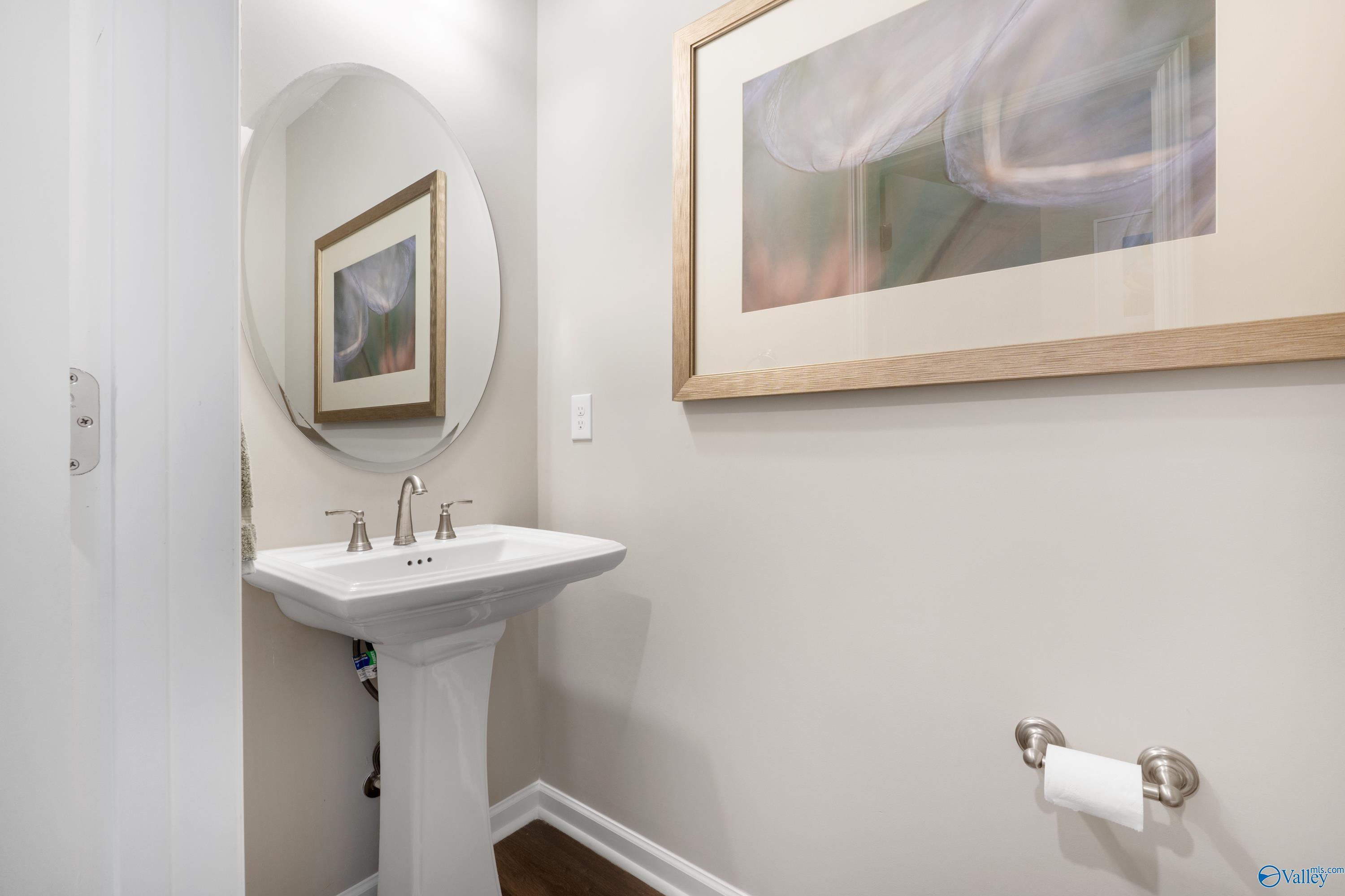Elegant powder room with white pedestal sink, round mirror, abstract tulip art, and chrome fixtures in Davidson Homes The Stella, Madison, Alabama